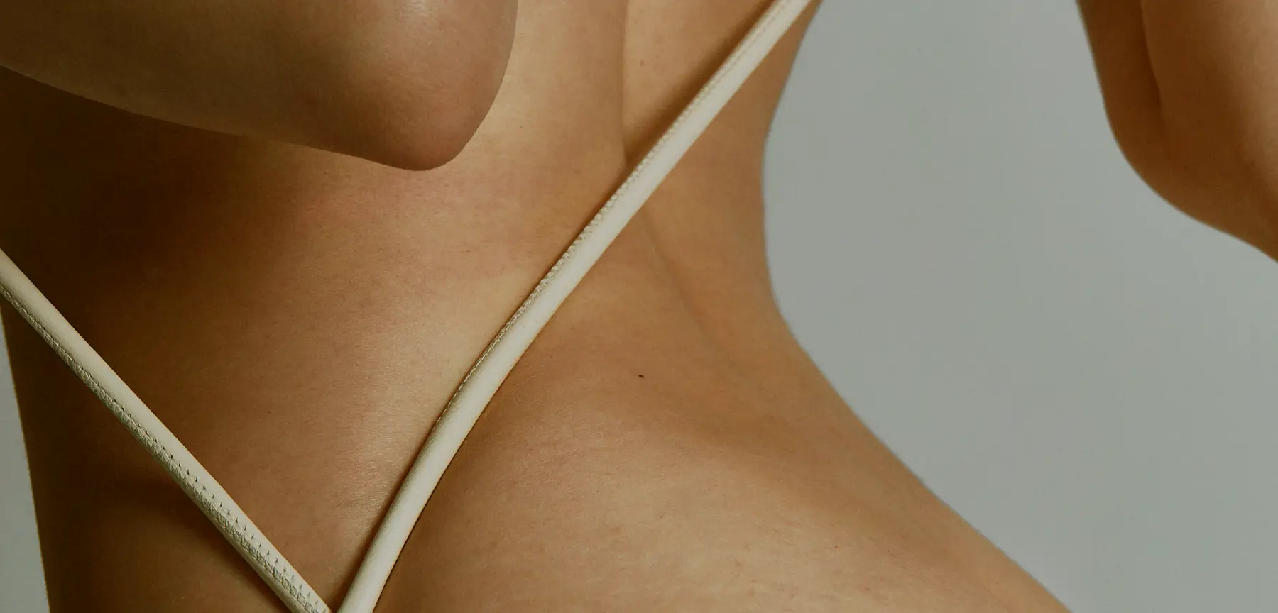 A close-up image showcasing the contours of a fit body adorned with a minimalist white swimsuit, emphasizing themes of wellness and premium fitness recovery, set against a neutral background.