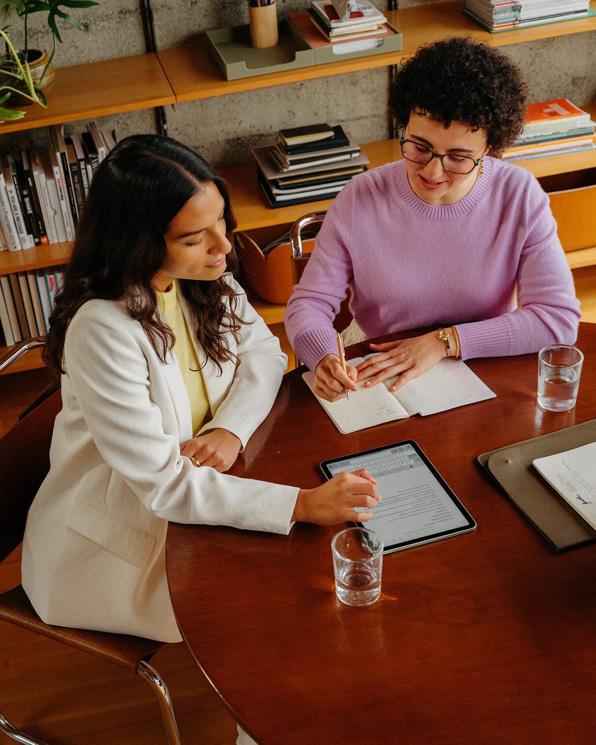 Man and woman standing together at a desk with a laptop and notebooks, smiling at the camera.