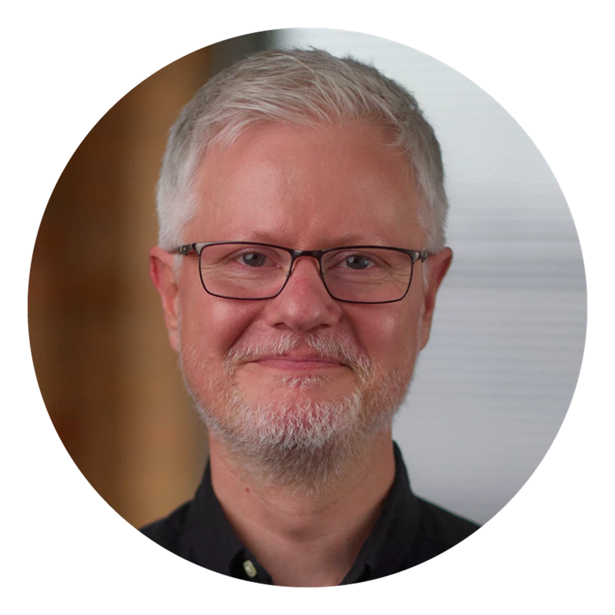  A circular portrait shows a person with short grey hair wearing a dark shirt. The background is softly lit and neutral.