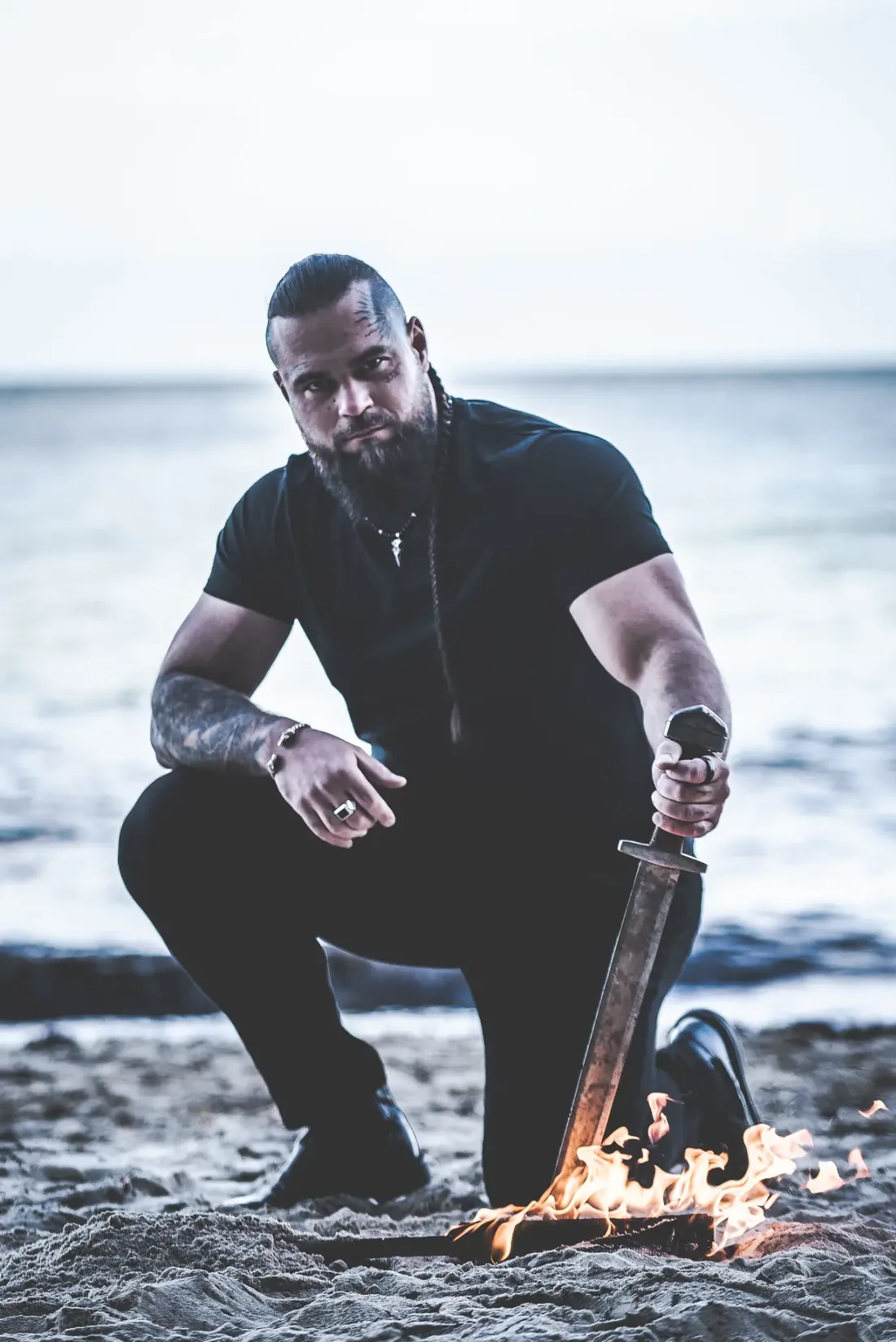 Paweł „Viking” Pawlak klęczy na plaży przy płonącym mieczu