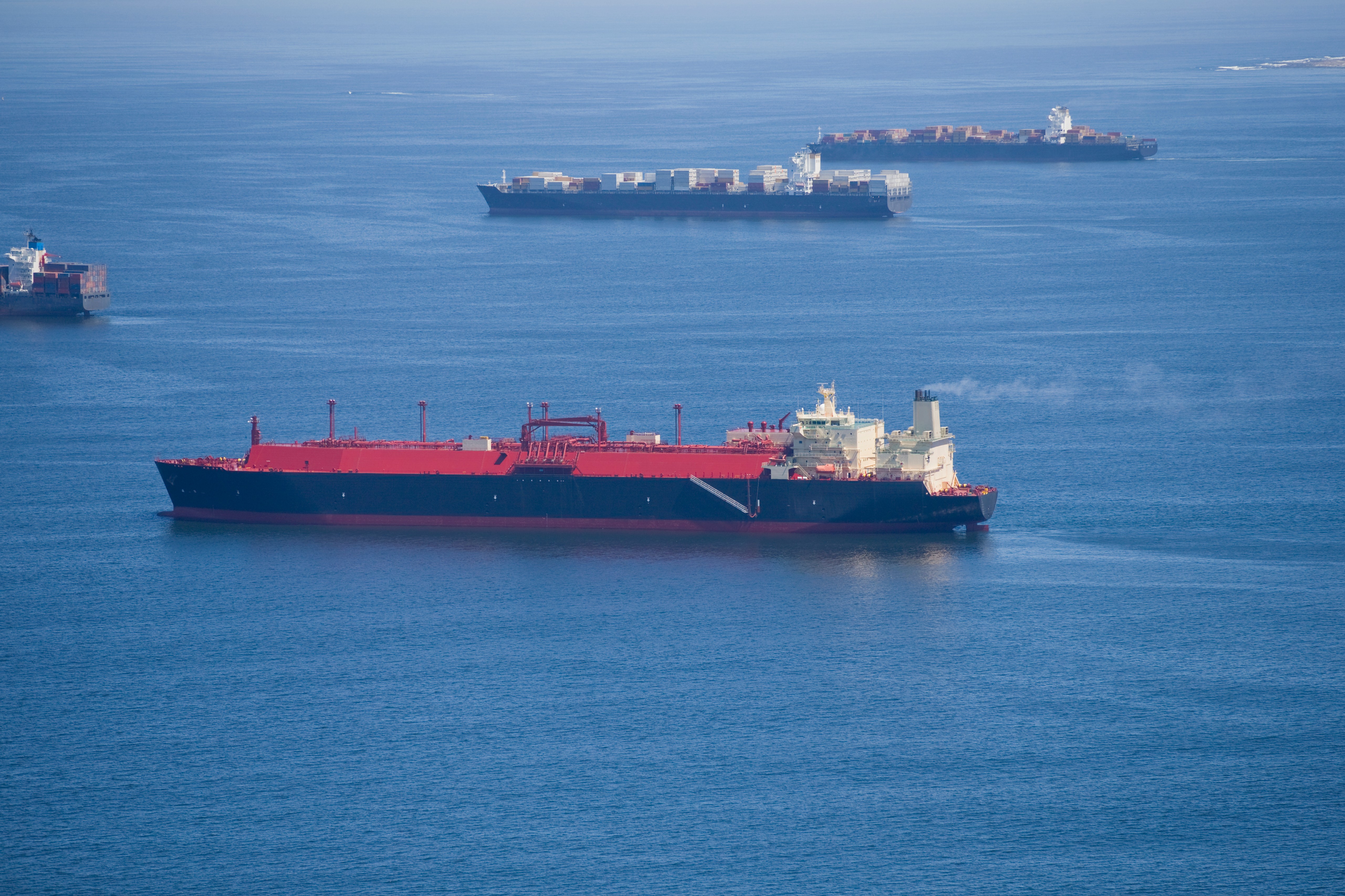 Side View Of A Natural Gas Cargo Ships Travelling At The Sea With Container Ships In The Background.