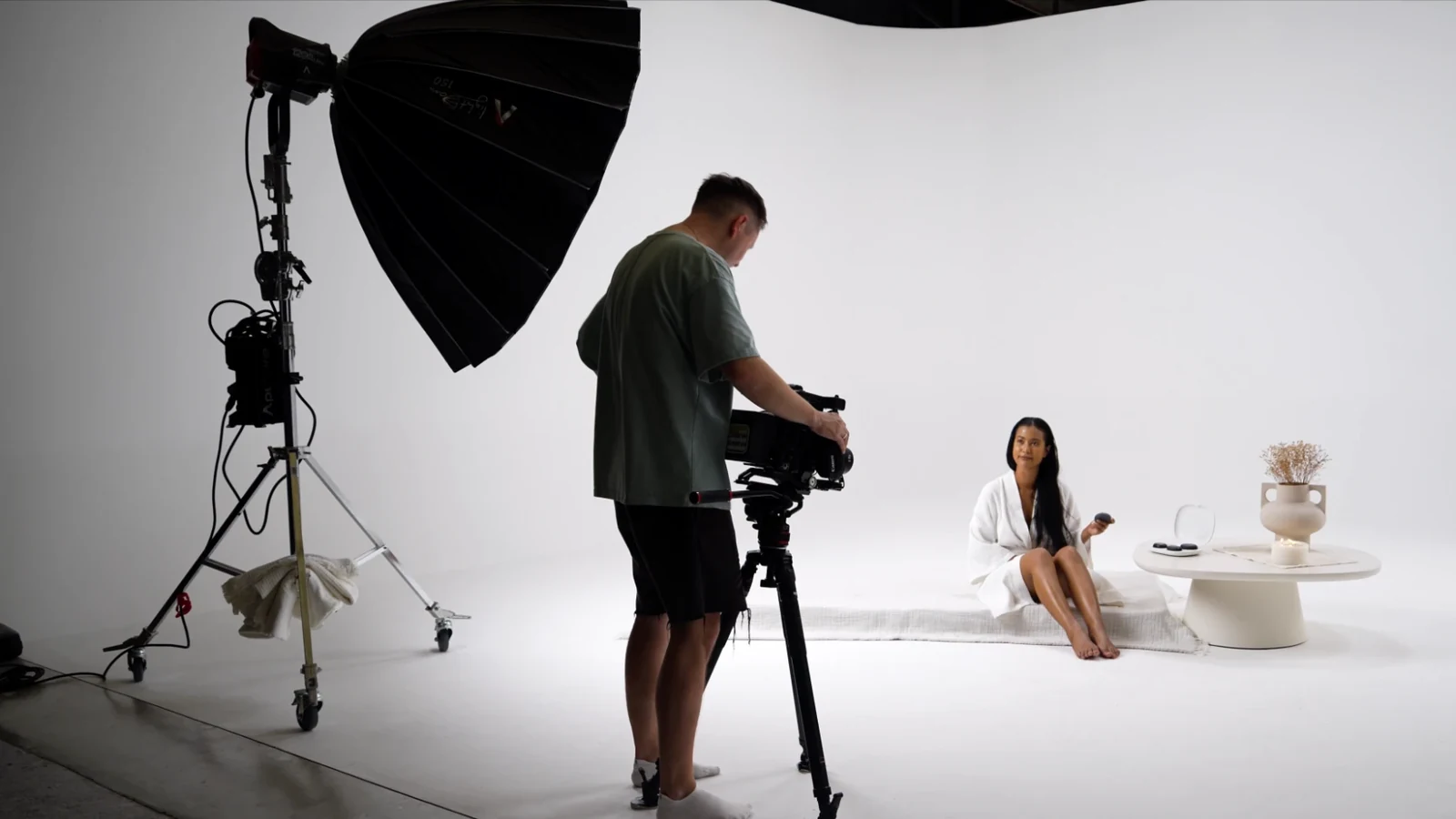 Camera operator filming the model in a white robe holding a heated stone