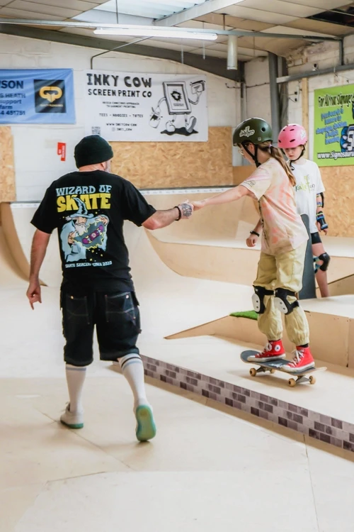 A skate coach helping a young girl on a skateboard at The Skate Farm indoor skatepark in Haywards Heath, Sussex