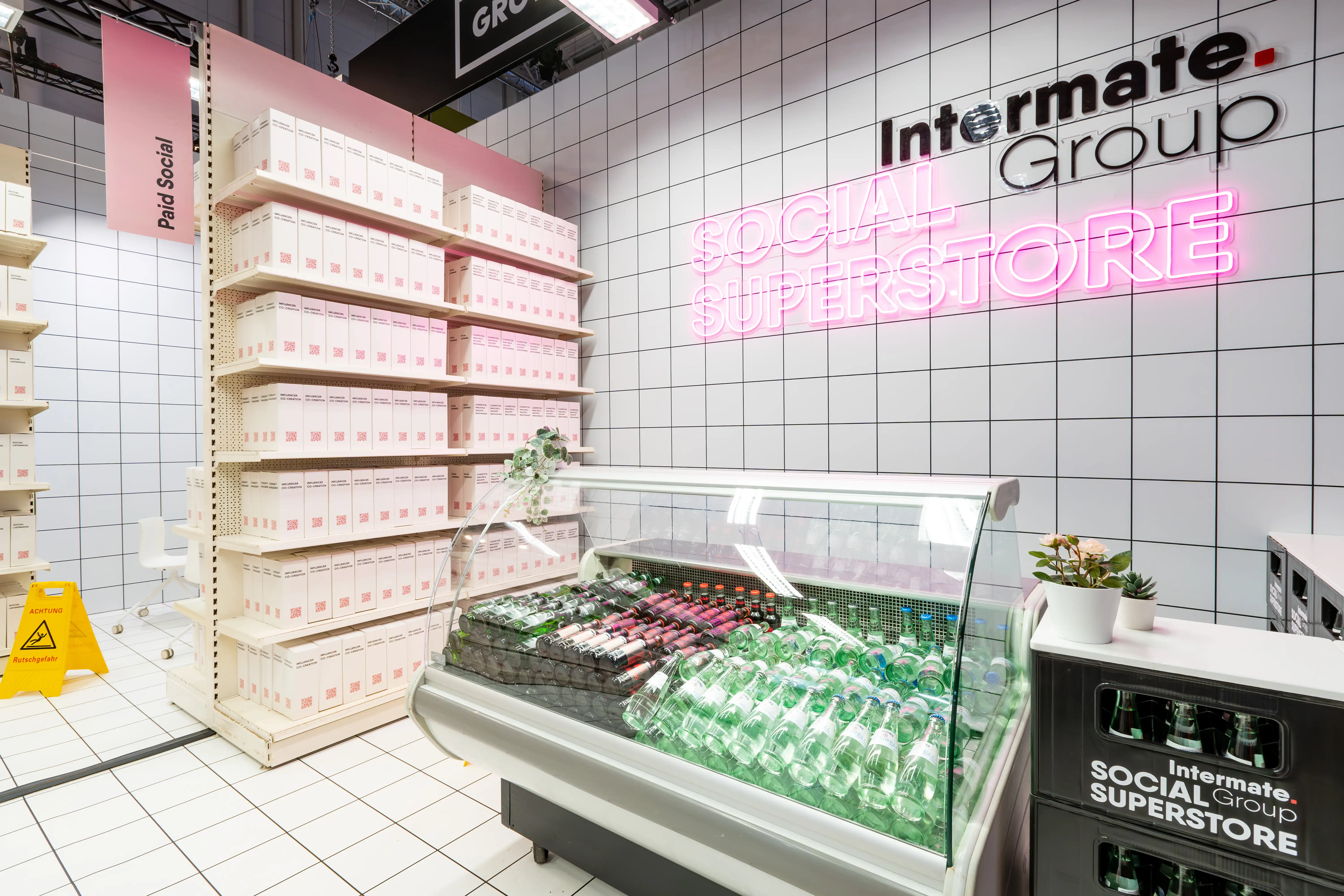 Refrigerated counter with drinks under the pink Social Superstore neon sign at the Intermate Group booth.