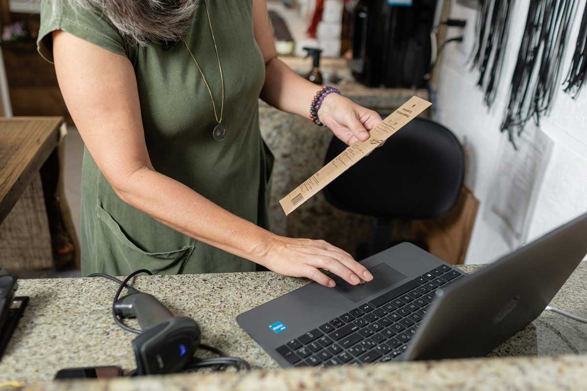 Mulher em ambiente de loja usando um notebook enquanto segura um produto.