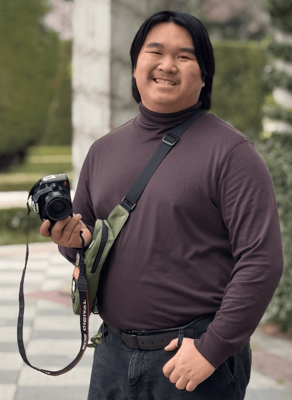 Photo of Evan Saisenesouk holding a Canon XSI Rebel camera in an outdoor garden in Madrid