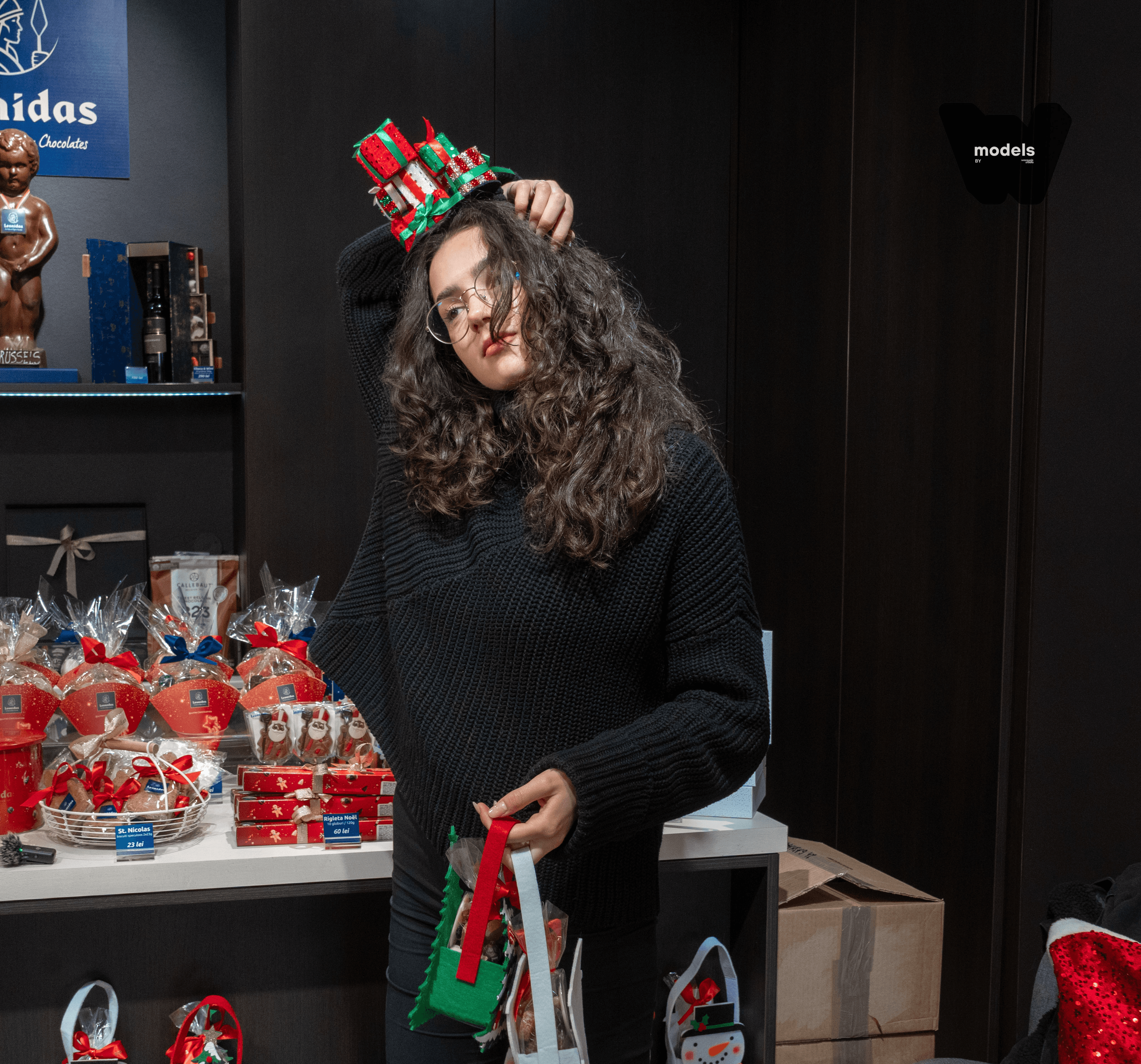 A smiling young man with crossed arms, wearing a plaid shirt and white t-shirt, poses against a dark background.
