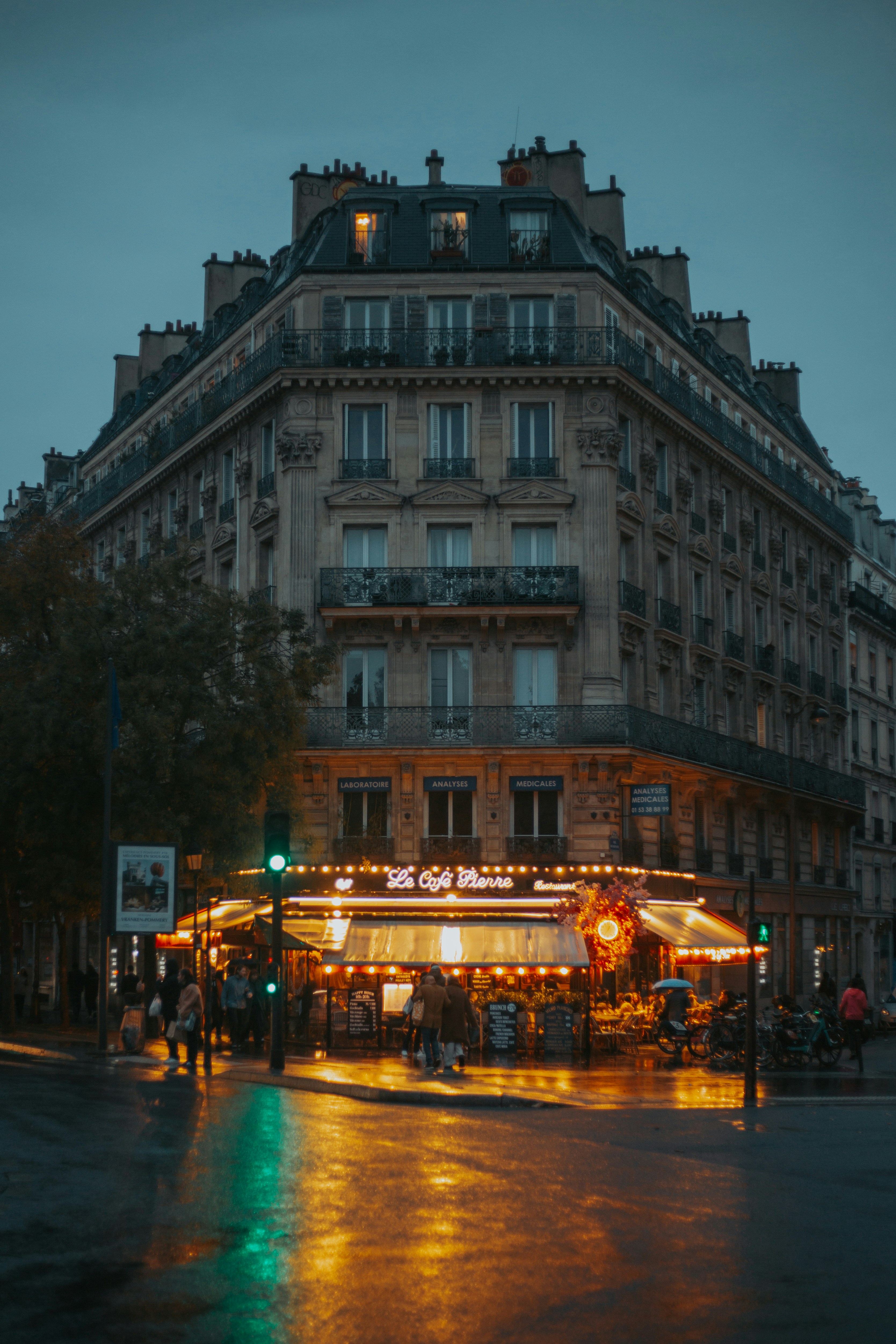 Corner building with a lit cafe on a wet street.