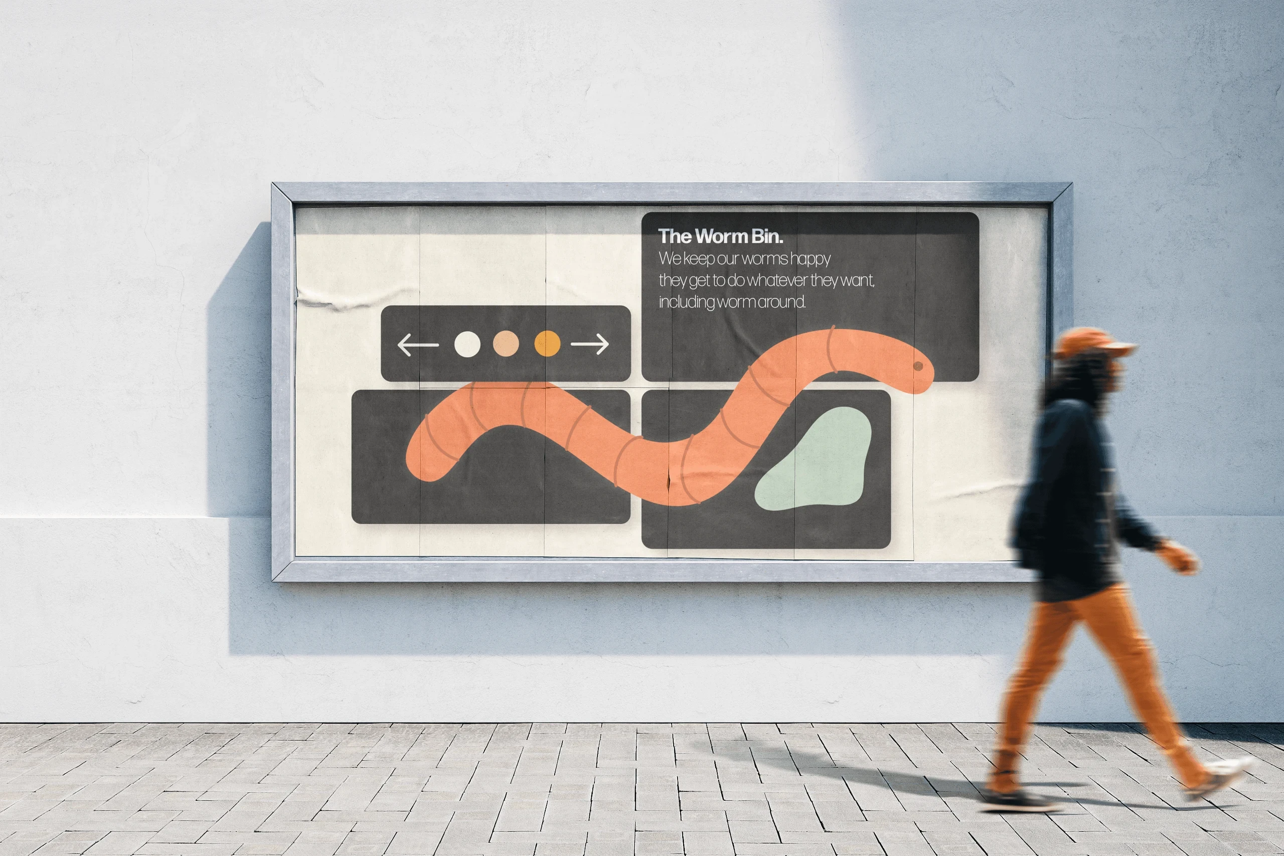 A wall-mounted poster case showing The Worm Bin campaign, an orange illustrated worm winding across dark panels, with a person in orange trousers walking past