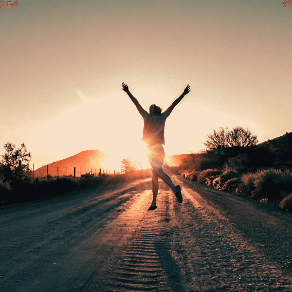 woman walking on a dirt road with her hands raised up with the sun