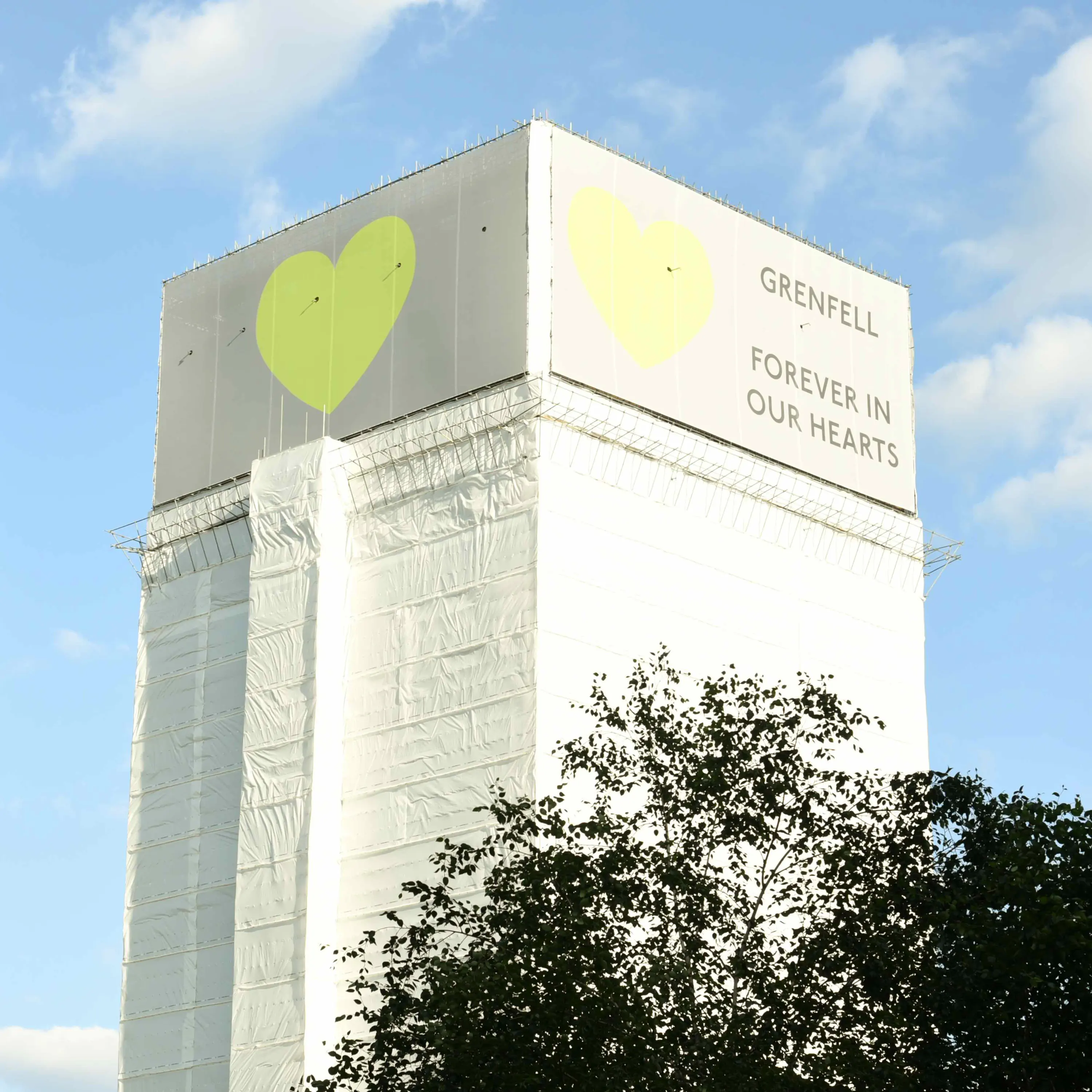 Grenfell Tower covered in mesh with the Green heart at the top and the text: "Forever in our hearts"