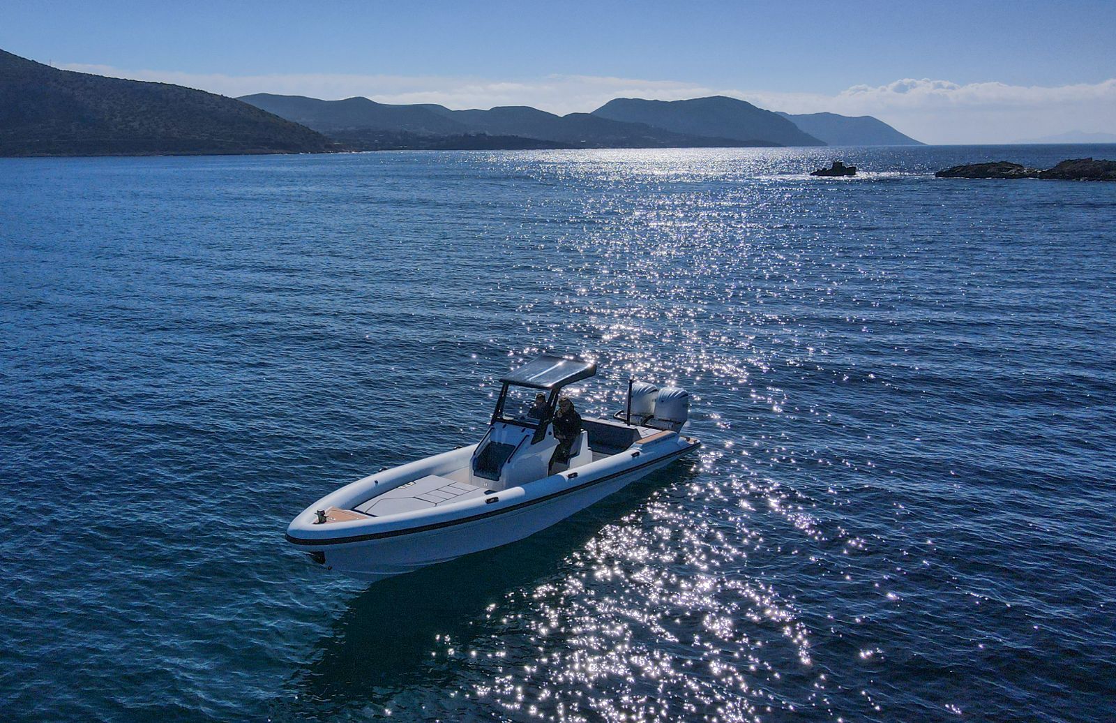 White Rock 36 speedboat with captain at helm cruising calm blue waters near Paros coastline with hills in background.