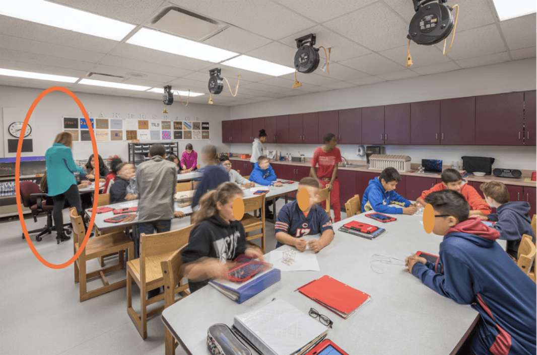 A teacher is interacting with a student in the class, while the others work independently.