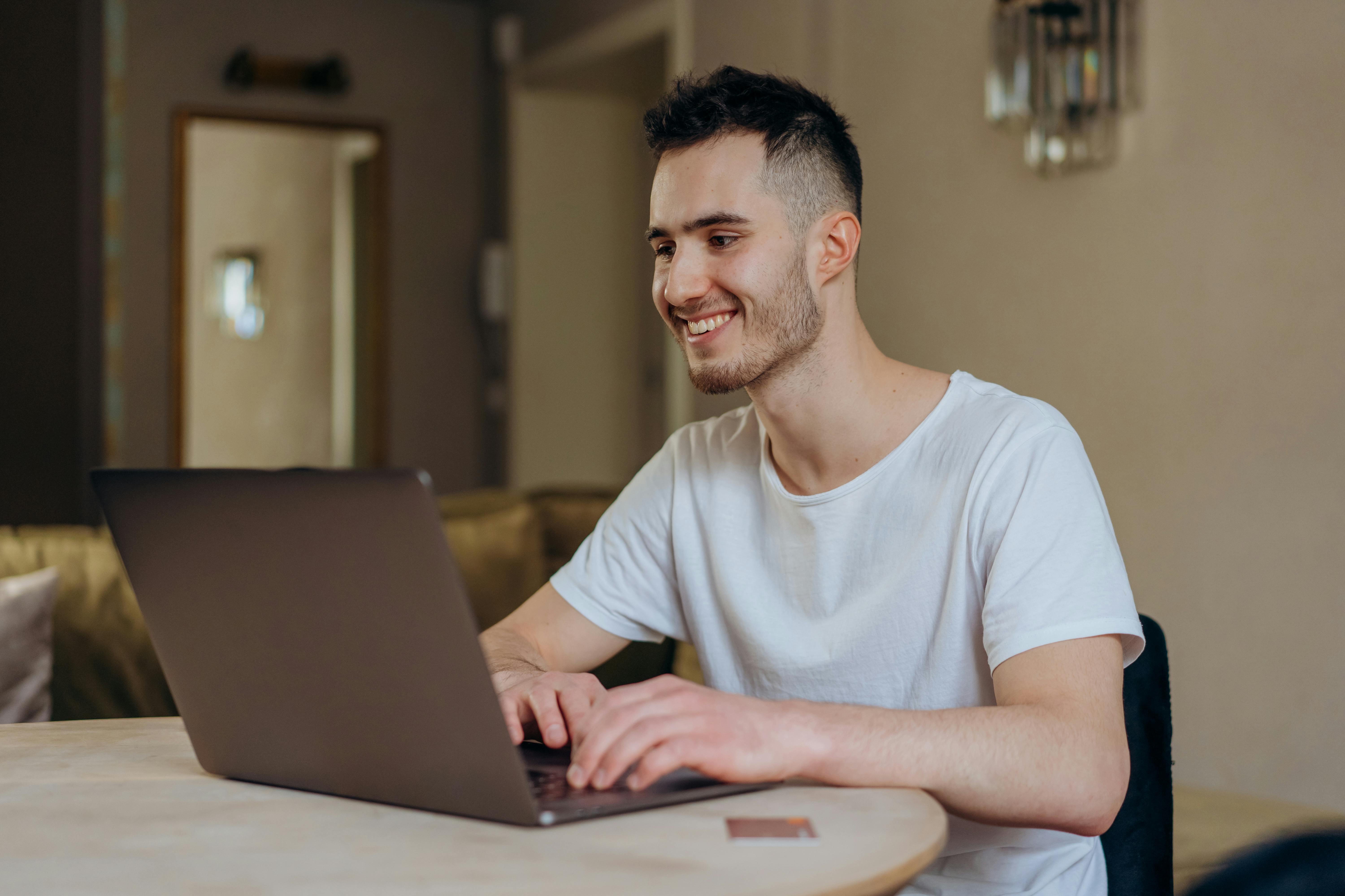 A man smiling at his laptop while working, representing how clear user journeys and strategic site improvements can increase conversions