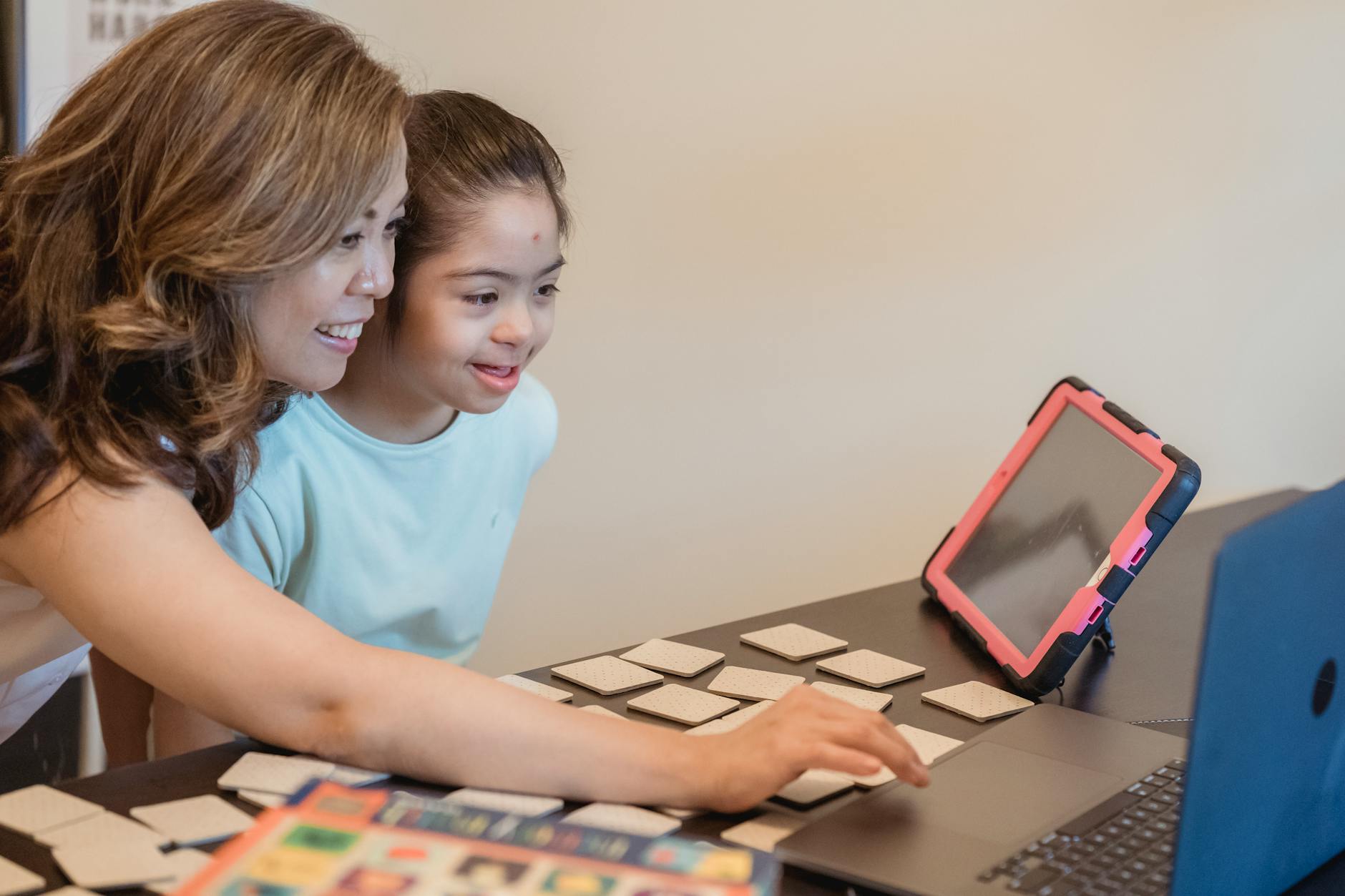 A mother and daughter sitting on a sofa looking at a tablet to review school grades and teacher feedback.
