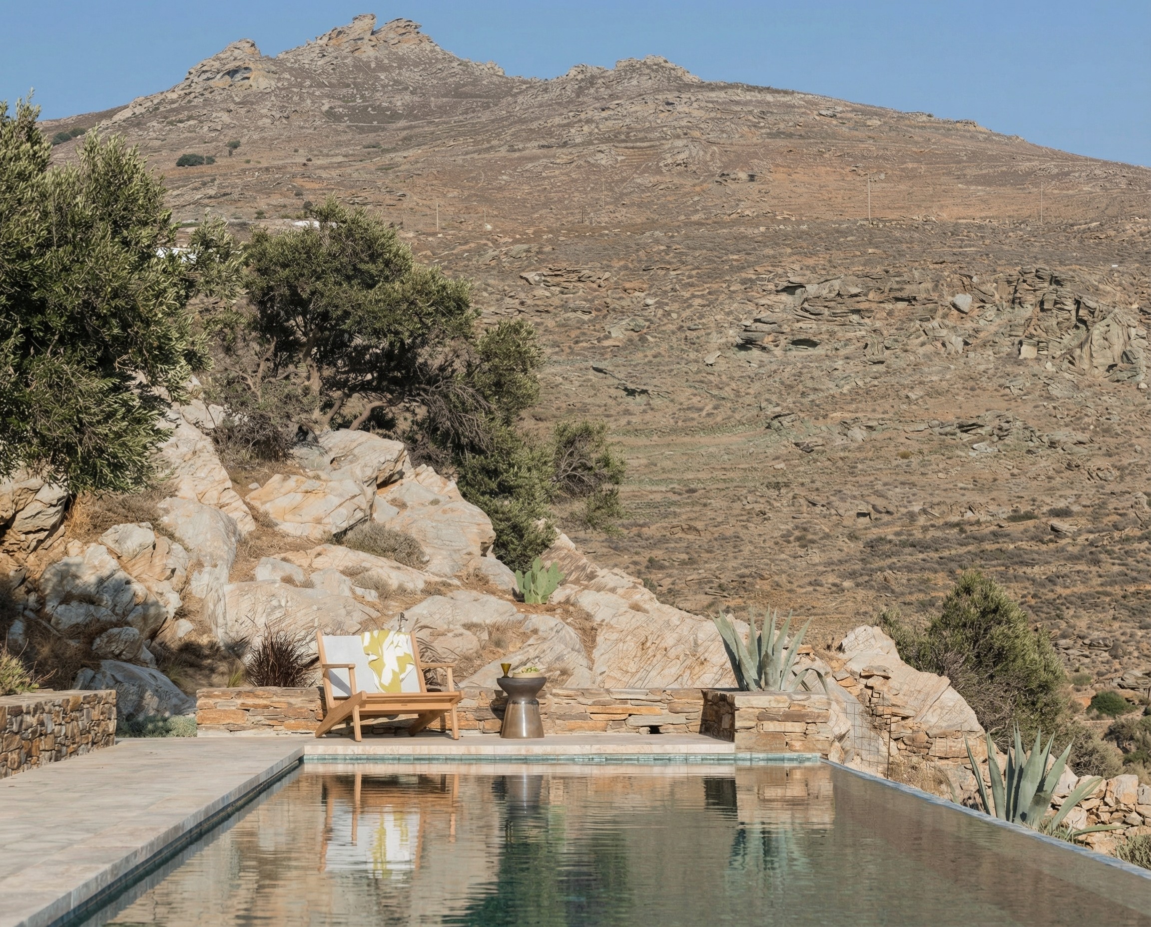 an infinity pool of a rural stay in front of a rocky hill by daytime