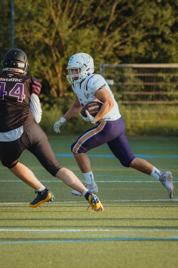 Ein Bucks-Spieler in Weiß läuft mit dem Ball über das Feld, ein Gegner in Dunkelviolett verfolgt ihn.