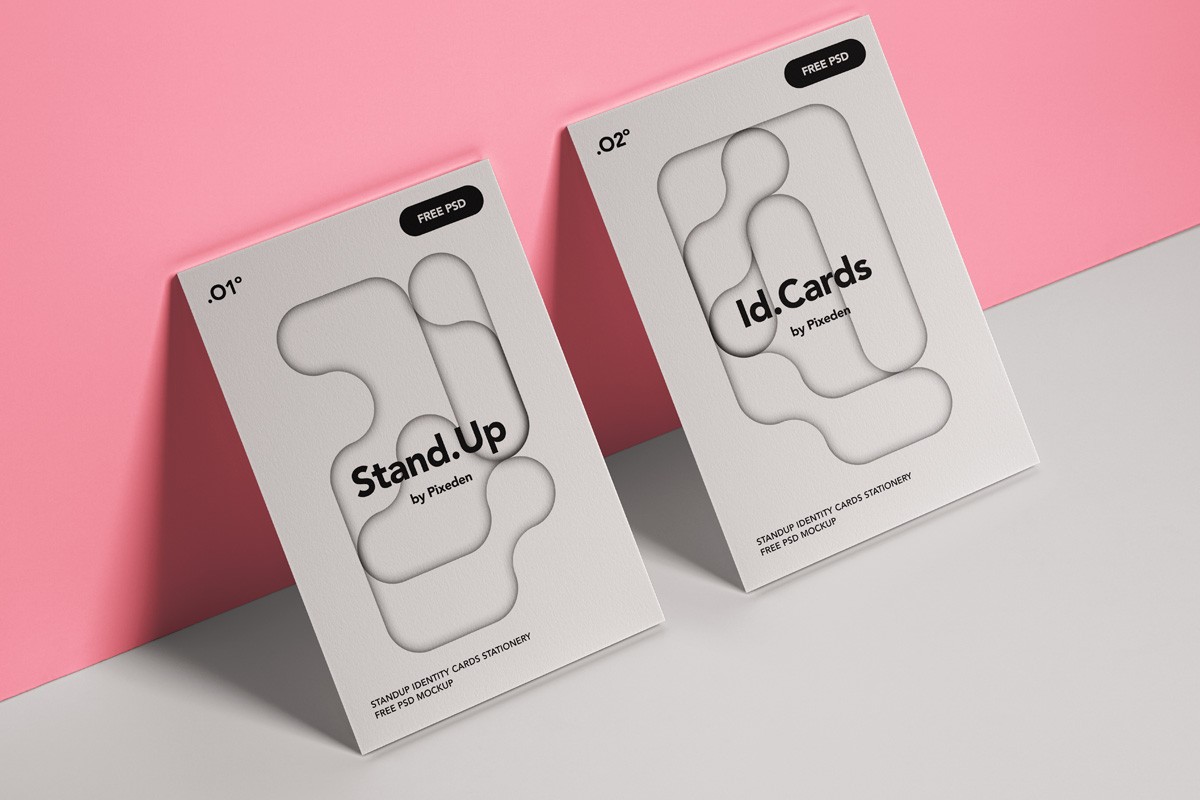 Two standing identity card mockups with abstract cutout designs on white backgrounds, leaning against a pink wall on a gray surface. Minimalist layout with soft lighting highlights the textures.