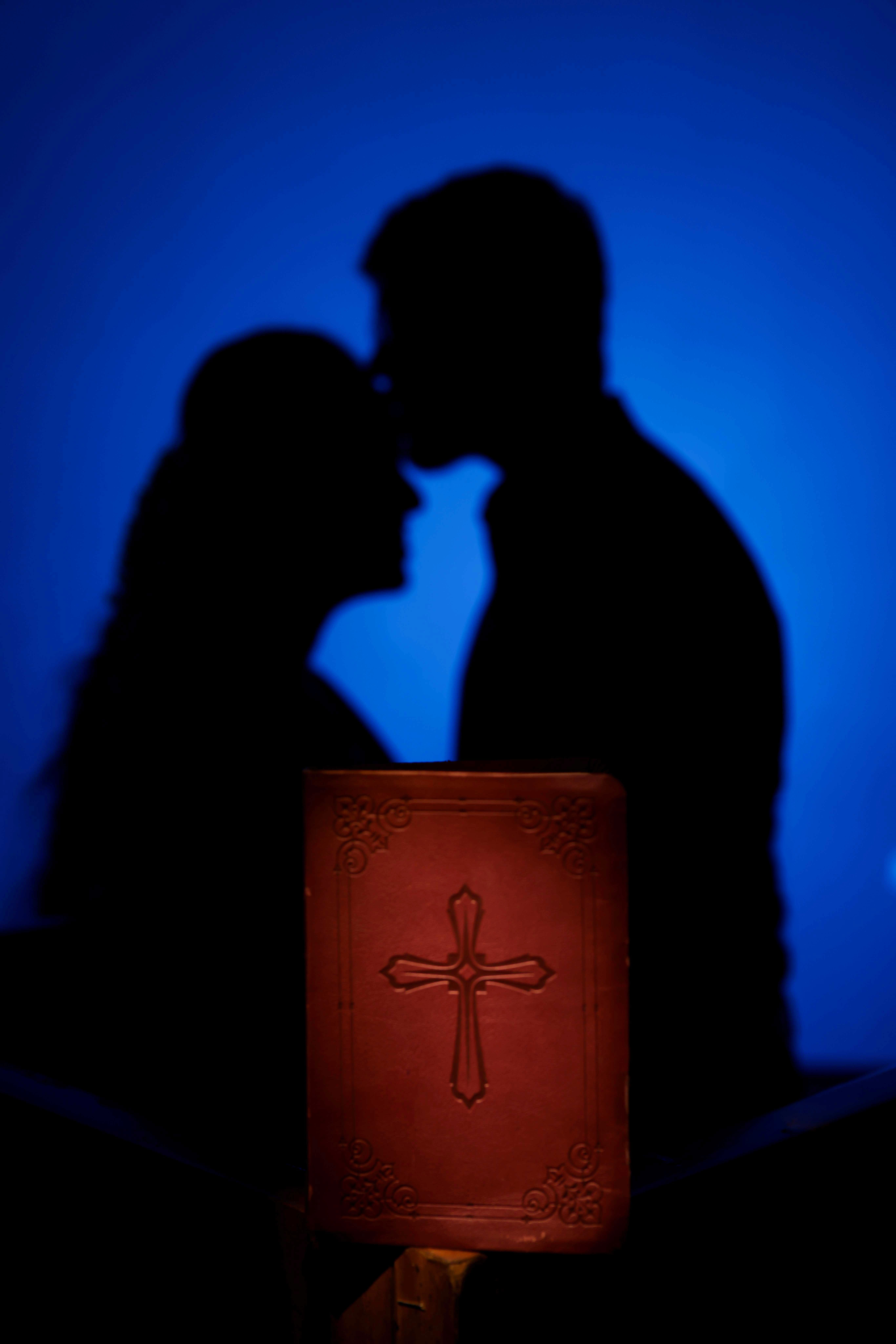 A close-up of two people holding hands, one wearing a denim jacket. The background is softly blurred, suggesting a tender, intimate moment in warm light.