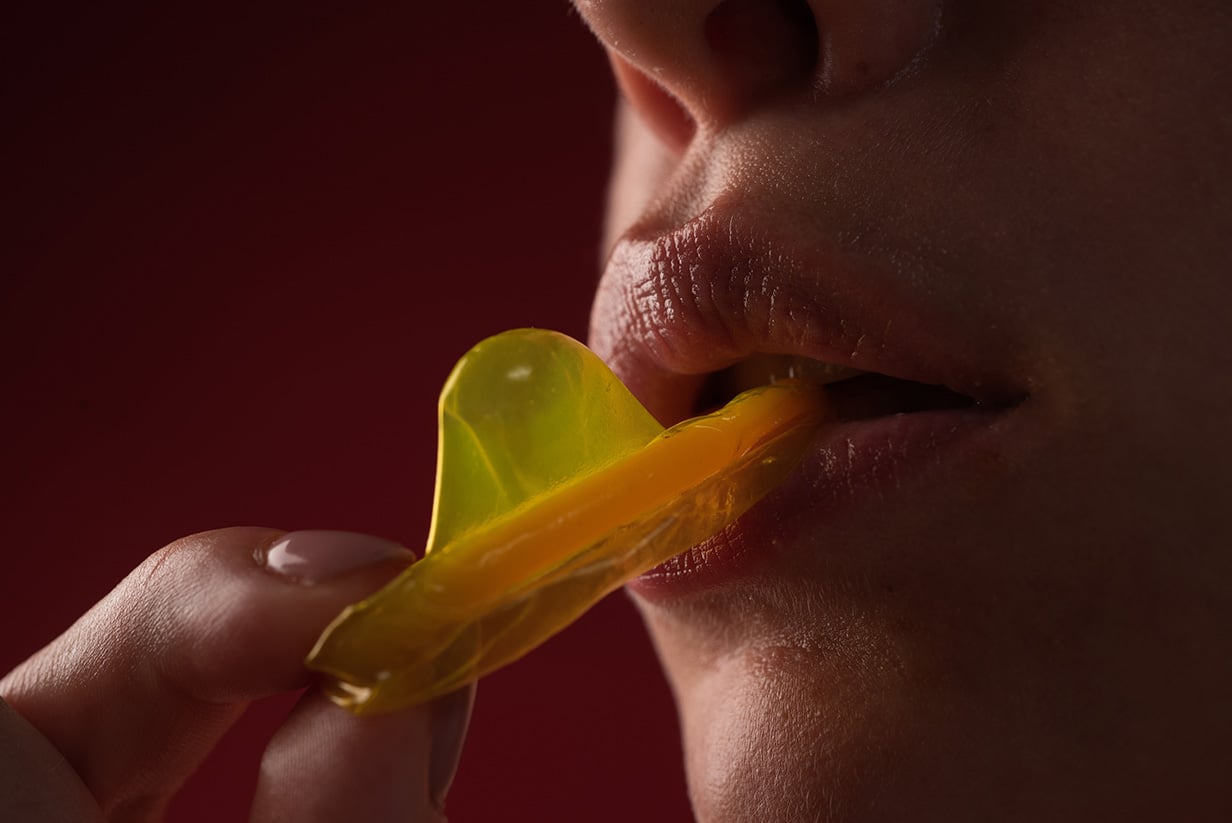 Mouth of a girl with tongue licking a condom