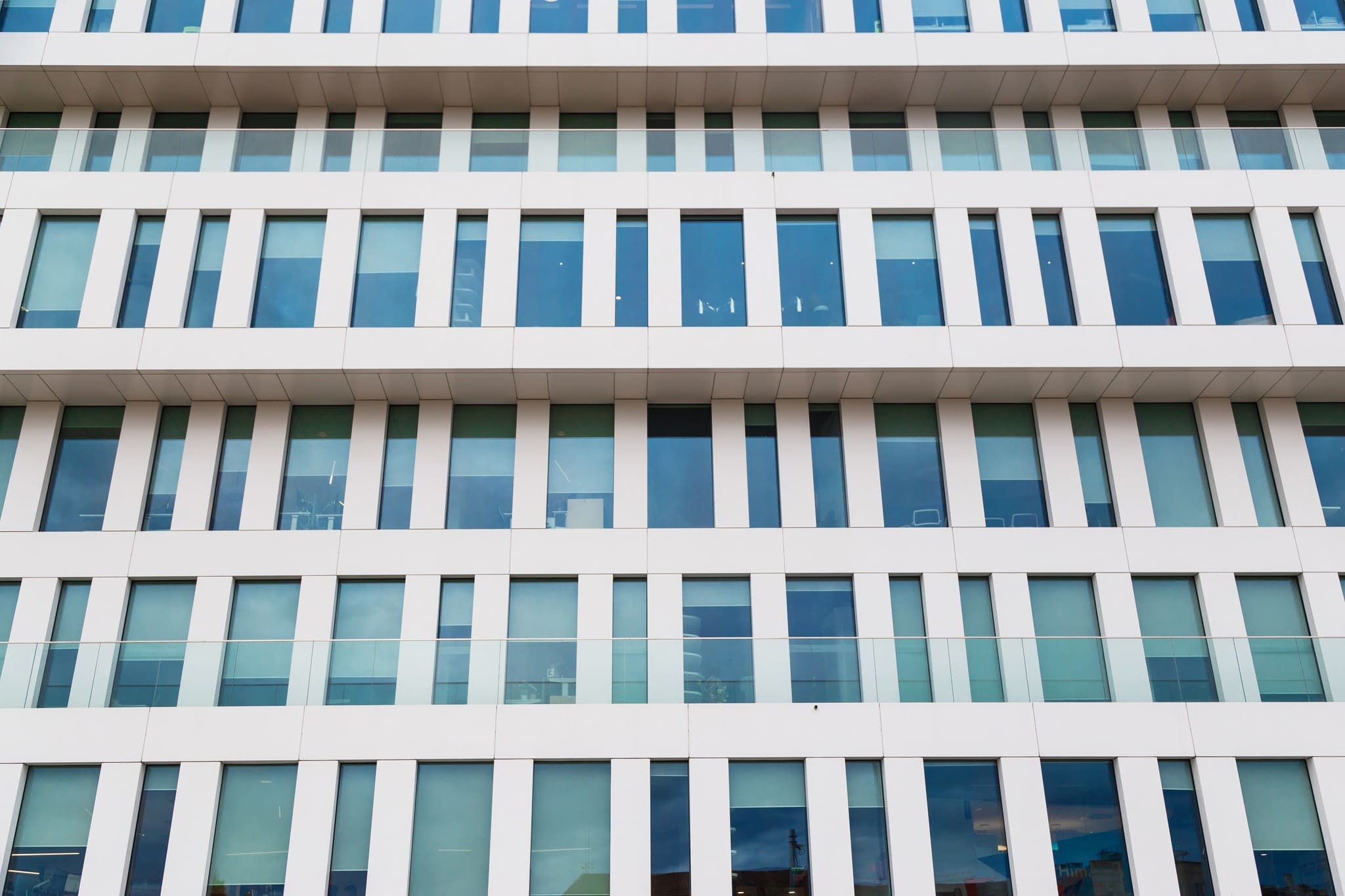 Straight-on view of a modern white building facade with symmetrical rows of glass windows.