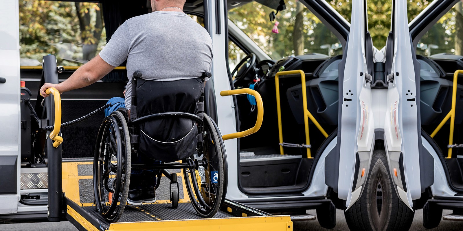 A man in a wheelchair using a hydraulic lift to board a white accessible van