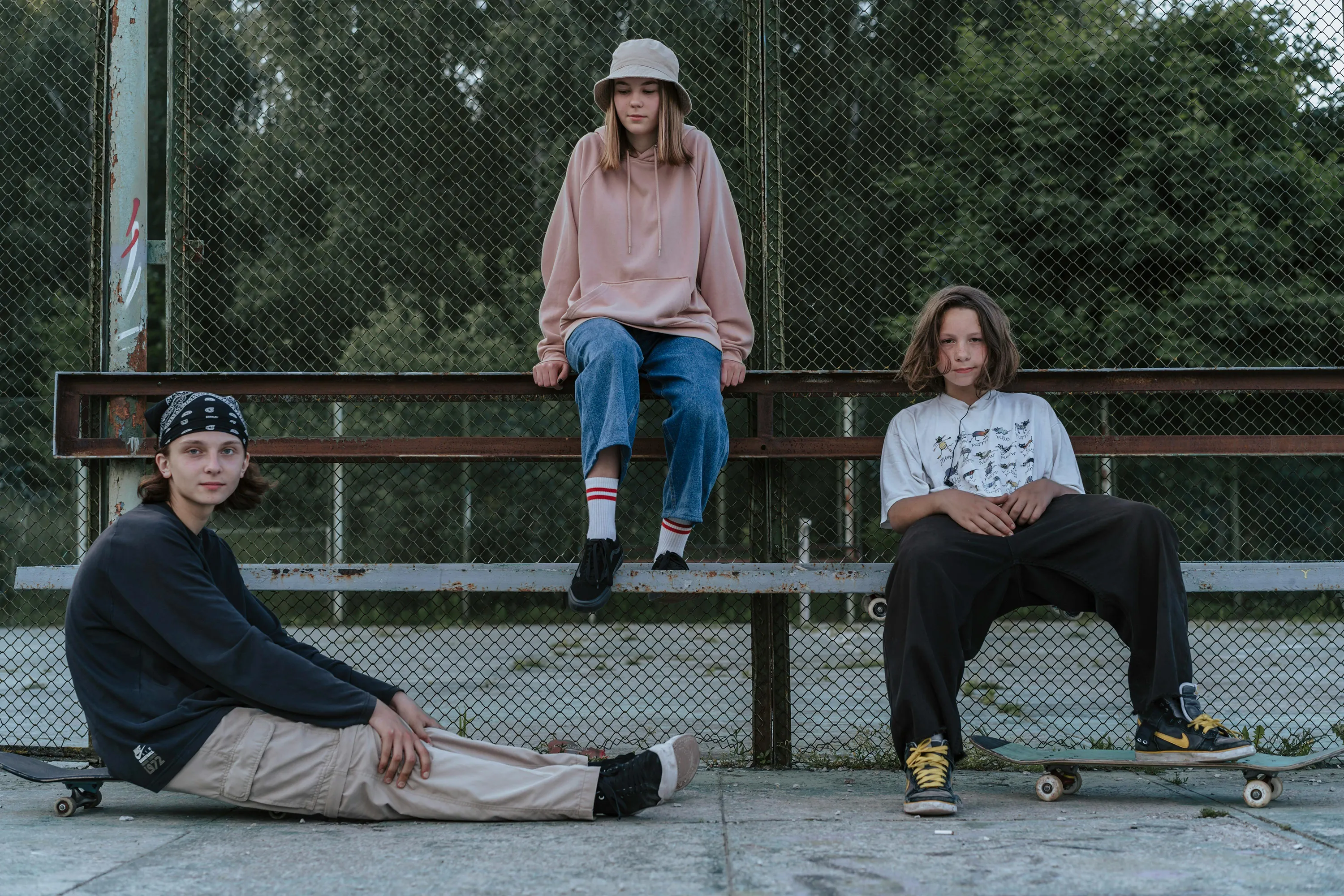 Three young people in streetwear hang out with their skateboards at a park