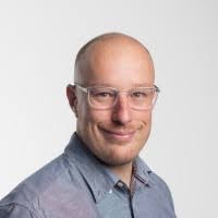 Portrait of a woman in a beige blazer with red lipstick, neutral background.