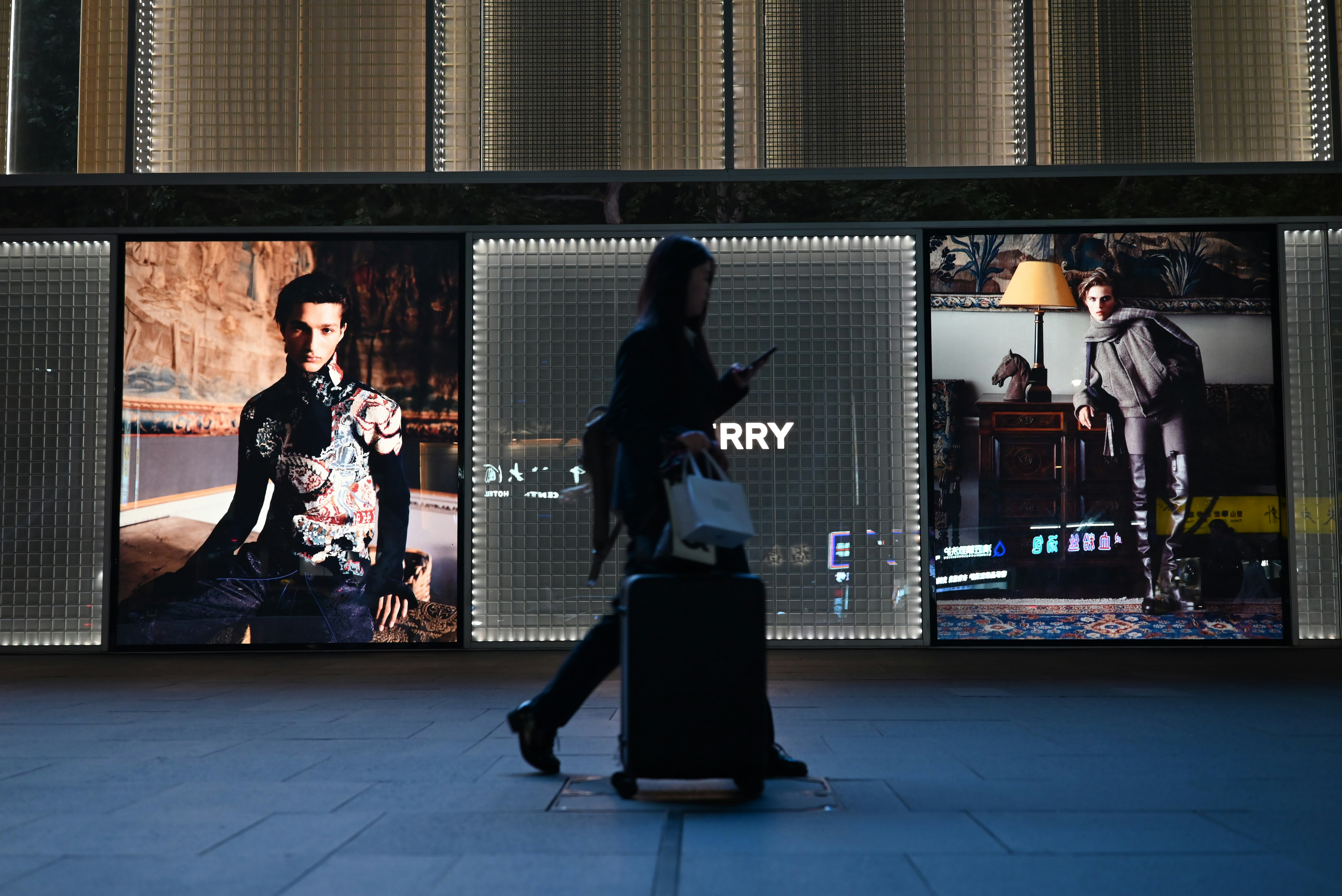 person-walks-past-illuminated-fashion-displays-at-night. - yingjie-wang (unsplash)./pho