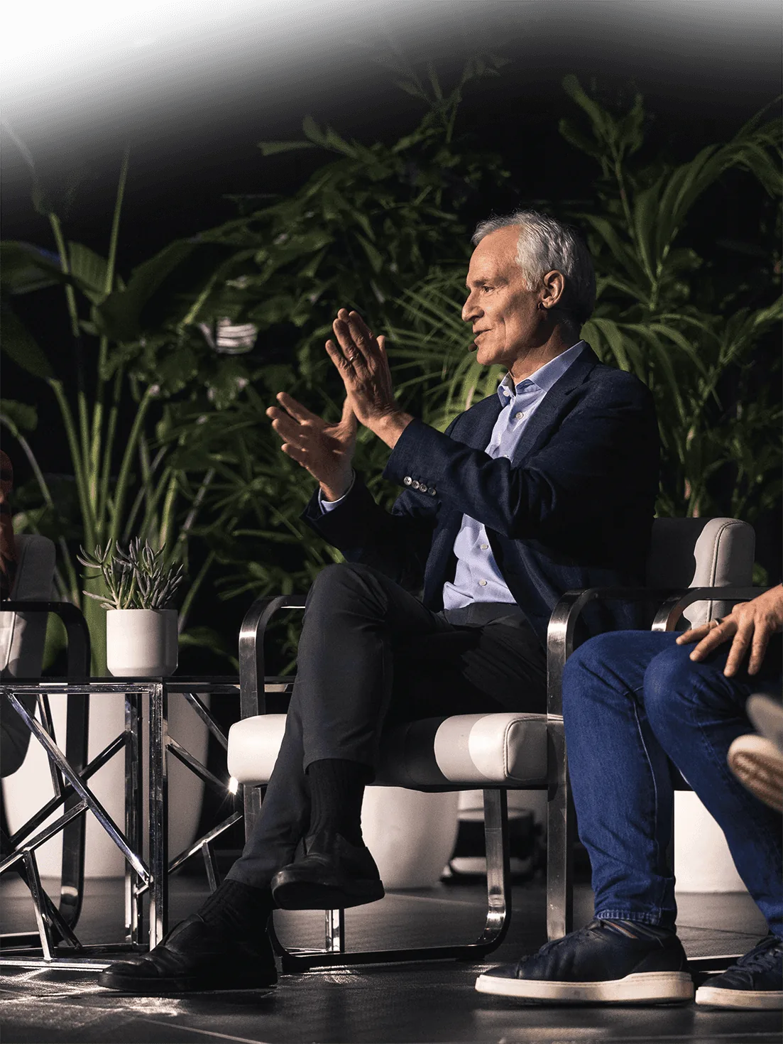Panelist in a navy blazer speaking on stage at SynBioBeta, framed by tropical plants