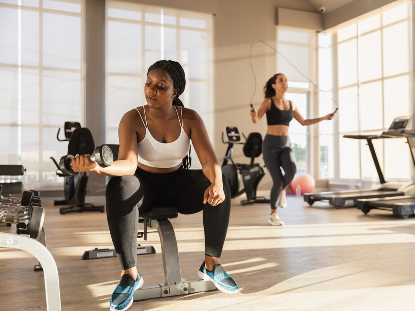 woman doing bicep curls with a dumbbell while sitting on a bench as part of her gym workout to lose weight