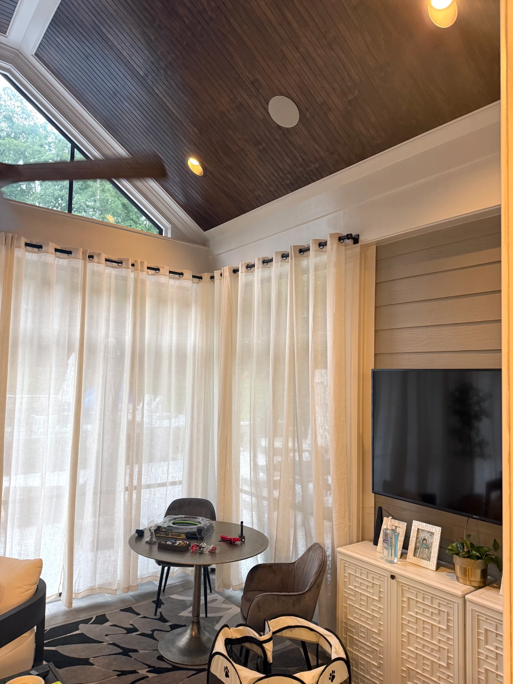 Sheer curtains frame a vaulted living room with a dark timber ceiling.