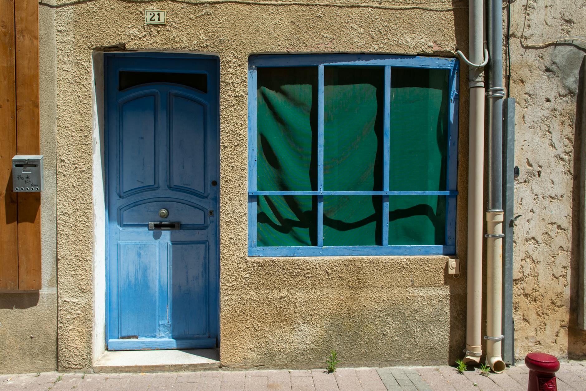 Blue painted front door numbered 21 alongside a green-curtained window on a weathered stone-faced terraced property