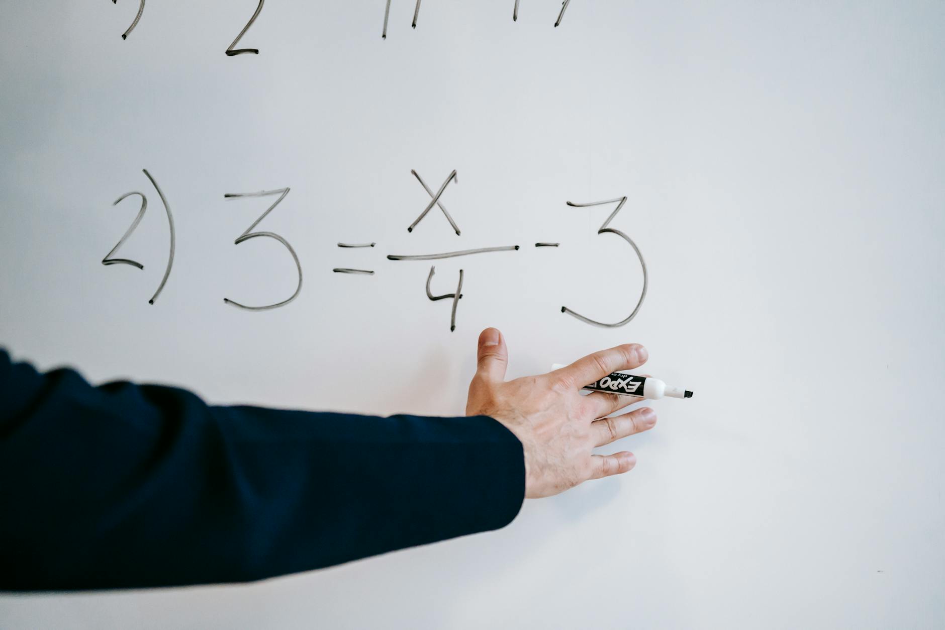 A teacher pointing at colorful geometric shapes on a whiteboard while explaining free math lesson plans to a class.