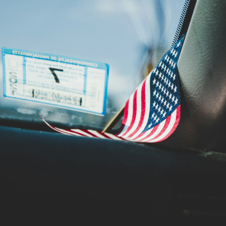 Close-up of a small American flag and a vehicle registration sticker on a car windshield.