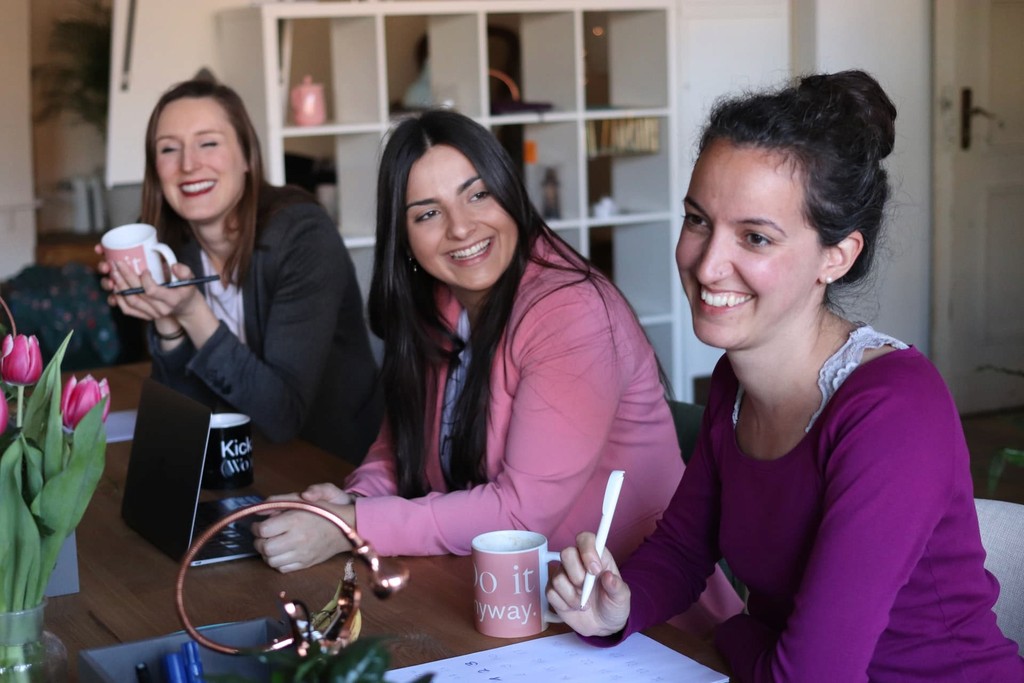 Smiling women in a meeting at an office table with coffee and tulips.