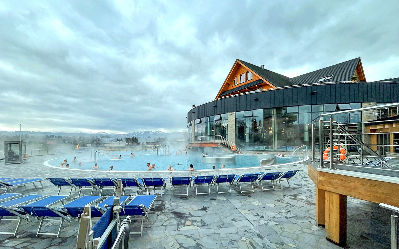 Outdoor pool at Zakopane Thermal Baths with people relaxing, surrounded by mountains.