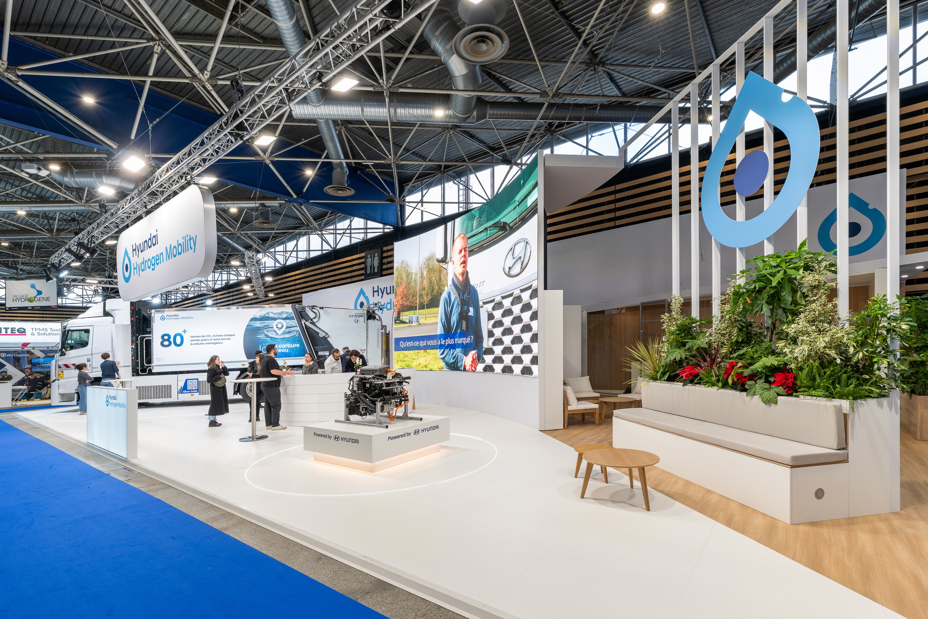Stand Hyundai Solutrans Lyon 2026 conçu par Expace – vue d'ensemble du stand ouvert avec zone exposition véhicules, décor végétal, structures modulaires bleues et blanches et sol blanc brillant