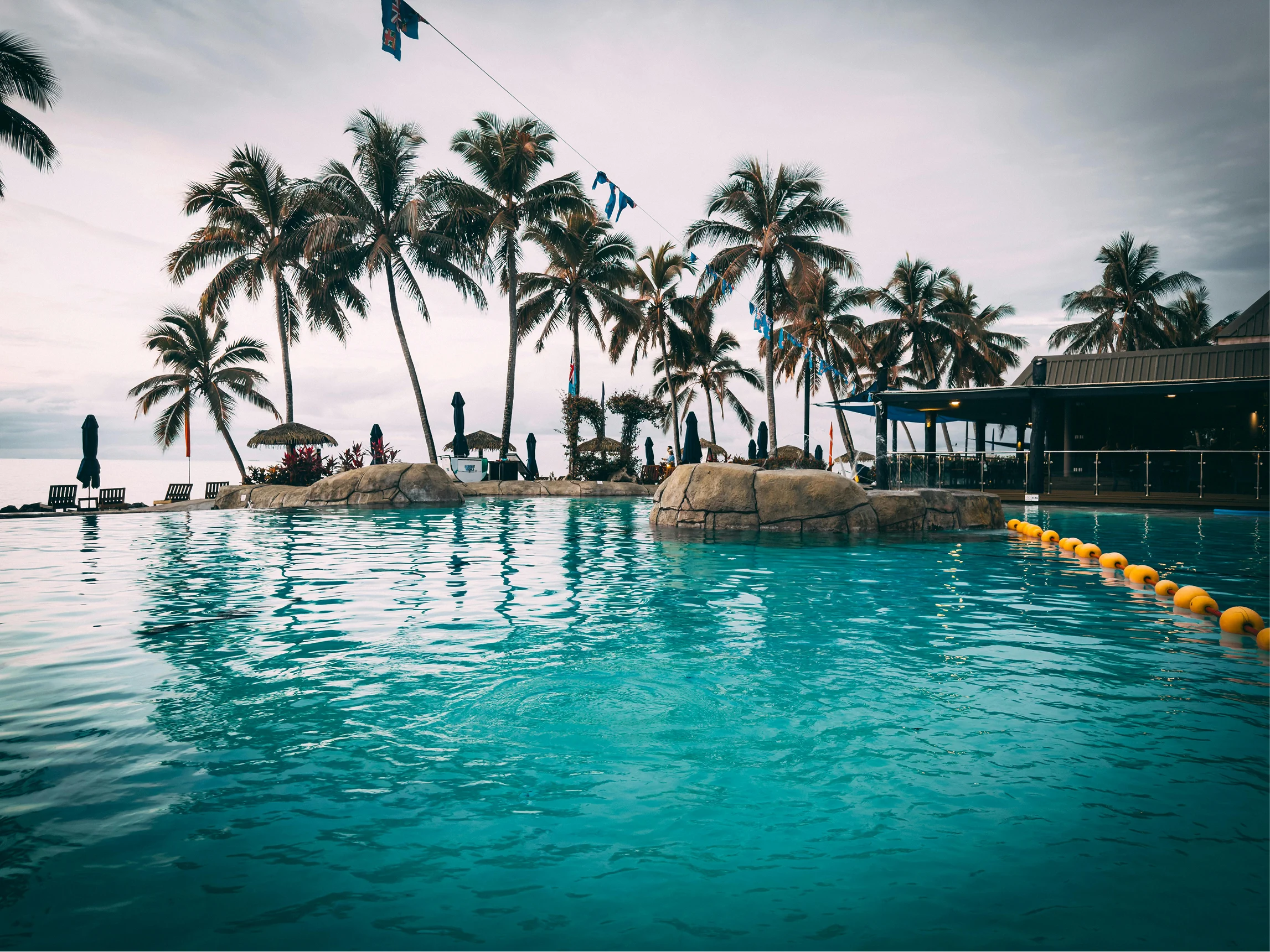 Beachfront swimming pool with palm trees and ocean views.