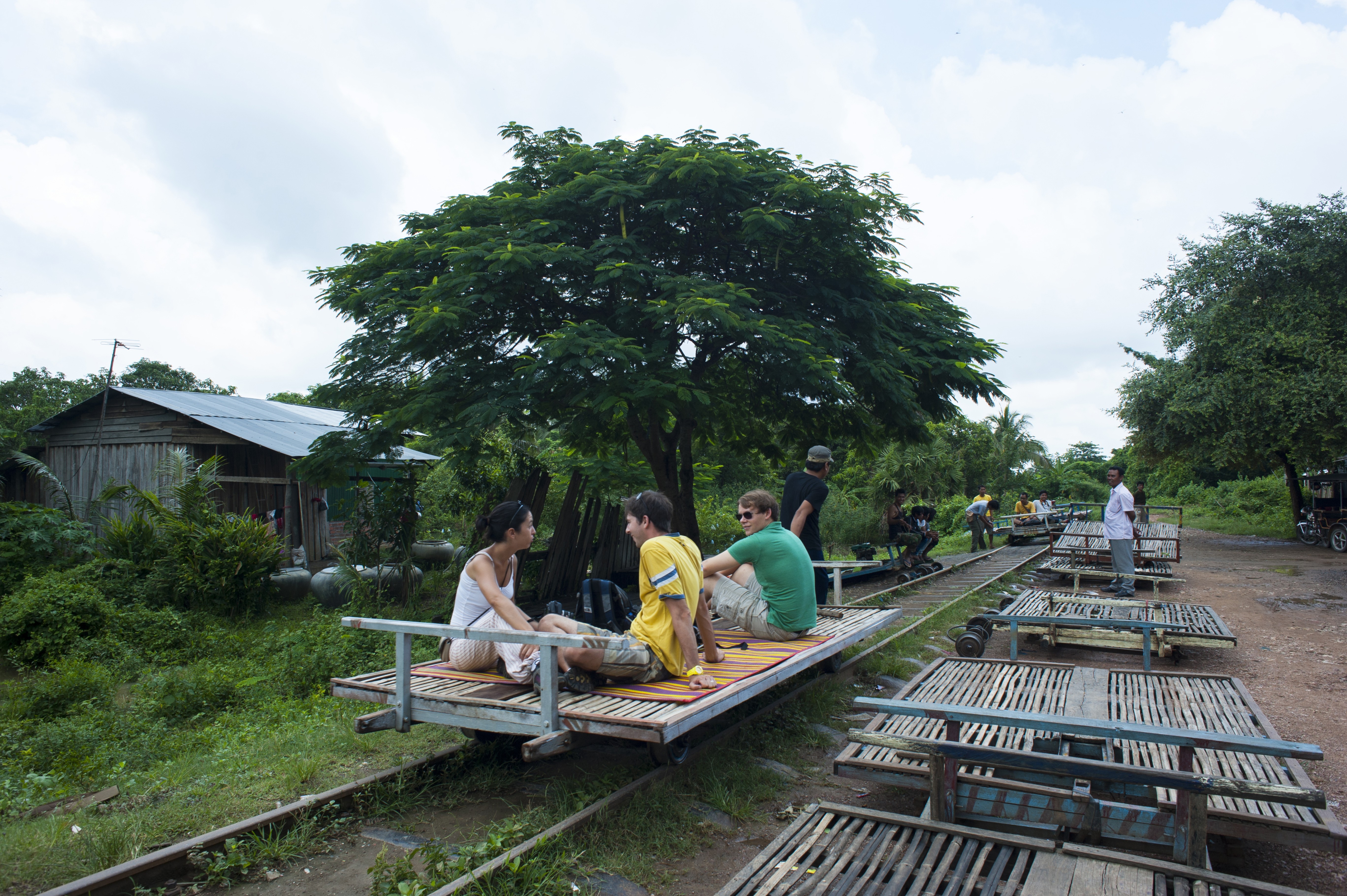 Three travelers sit on bamboo slats atop a simple wooden-framed train.