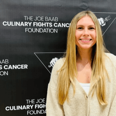 Portrait of Emily Tewksbury, MS, RDN, LD, smiling in front of a backdrop for The Joe Baab Culinary Fights Cancer Foundation.