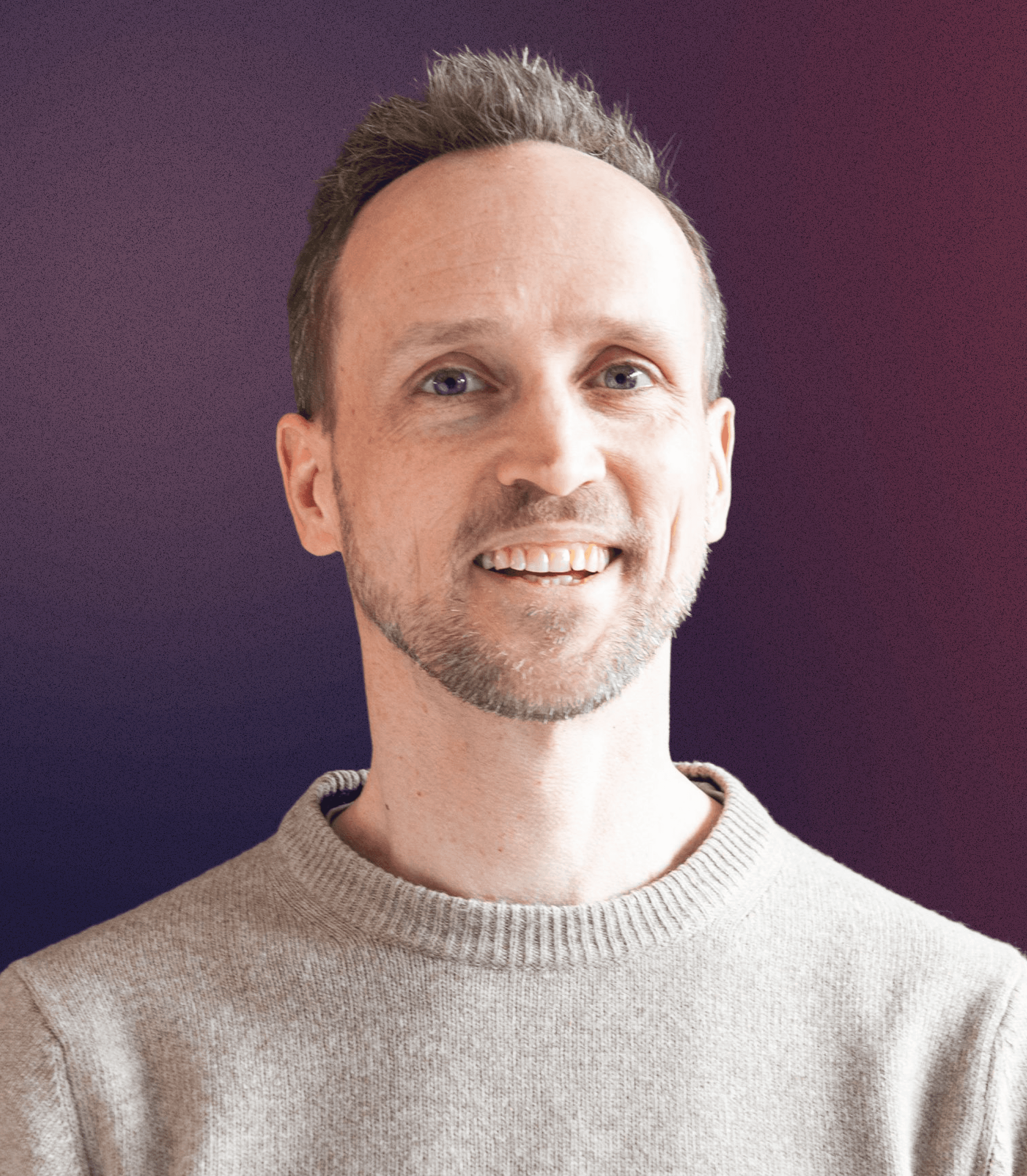 Portrait of a young man in a brown coat and beige turtleneck, with light brown hair and a calm expression against a gray background.