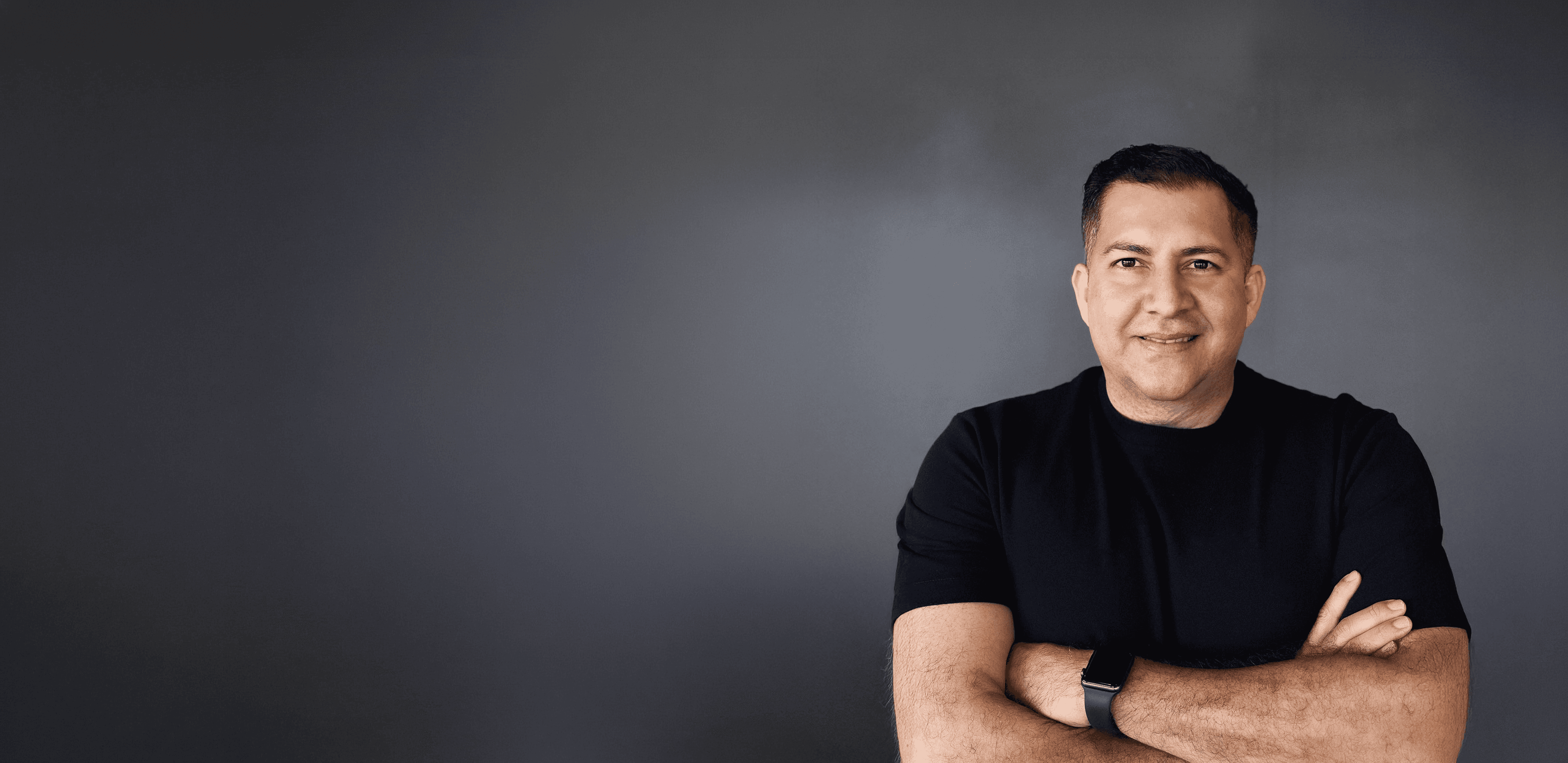 A man in a brown blazer and a woman in a light sweater sit at a desk with a laptop, discussing something. The room is dimly lit, creating a focused atmosphere.