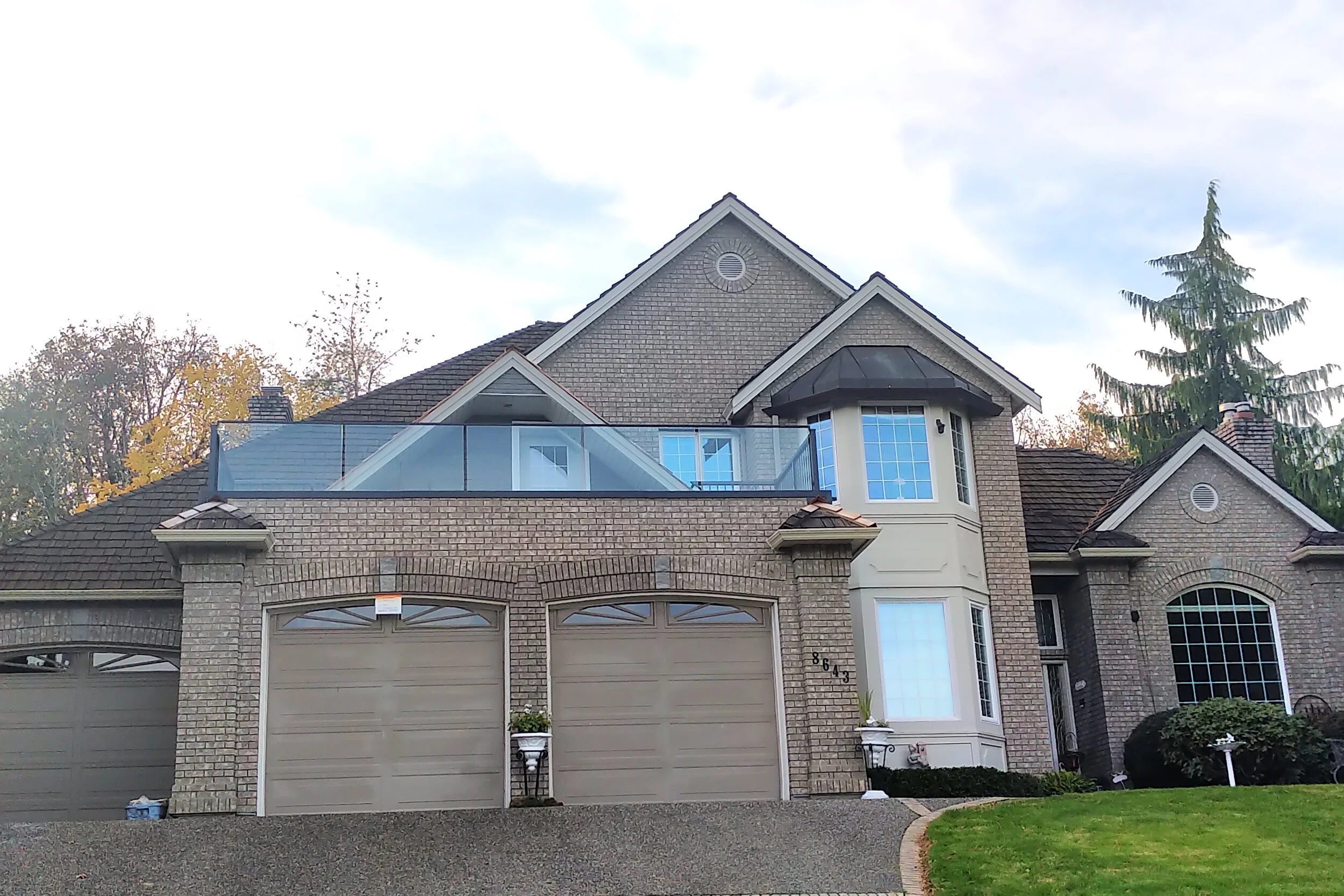 Residential exterior with glass balcony railing on brick façade, enhancing curb appeal and unobstructed views in Greater Vancouver.