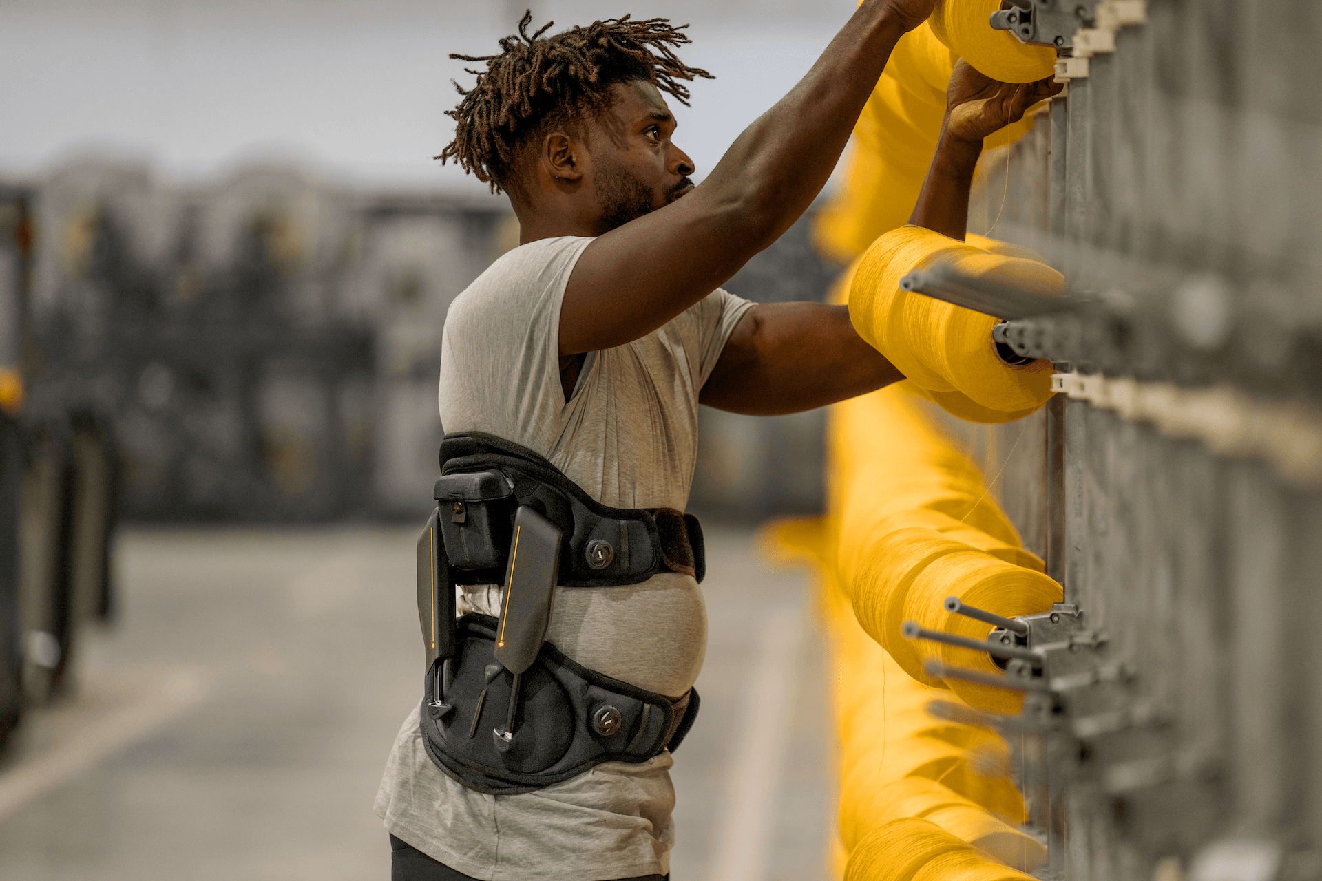 Industrial worker wearing back support exoskeleton (Japet.W+) to reduce strain during repetitive tasks in manufacturing environment