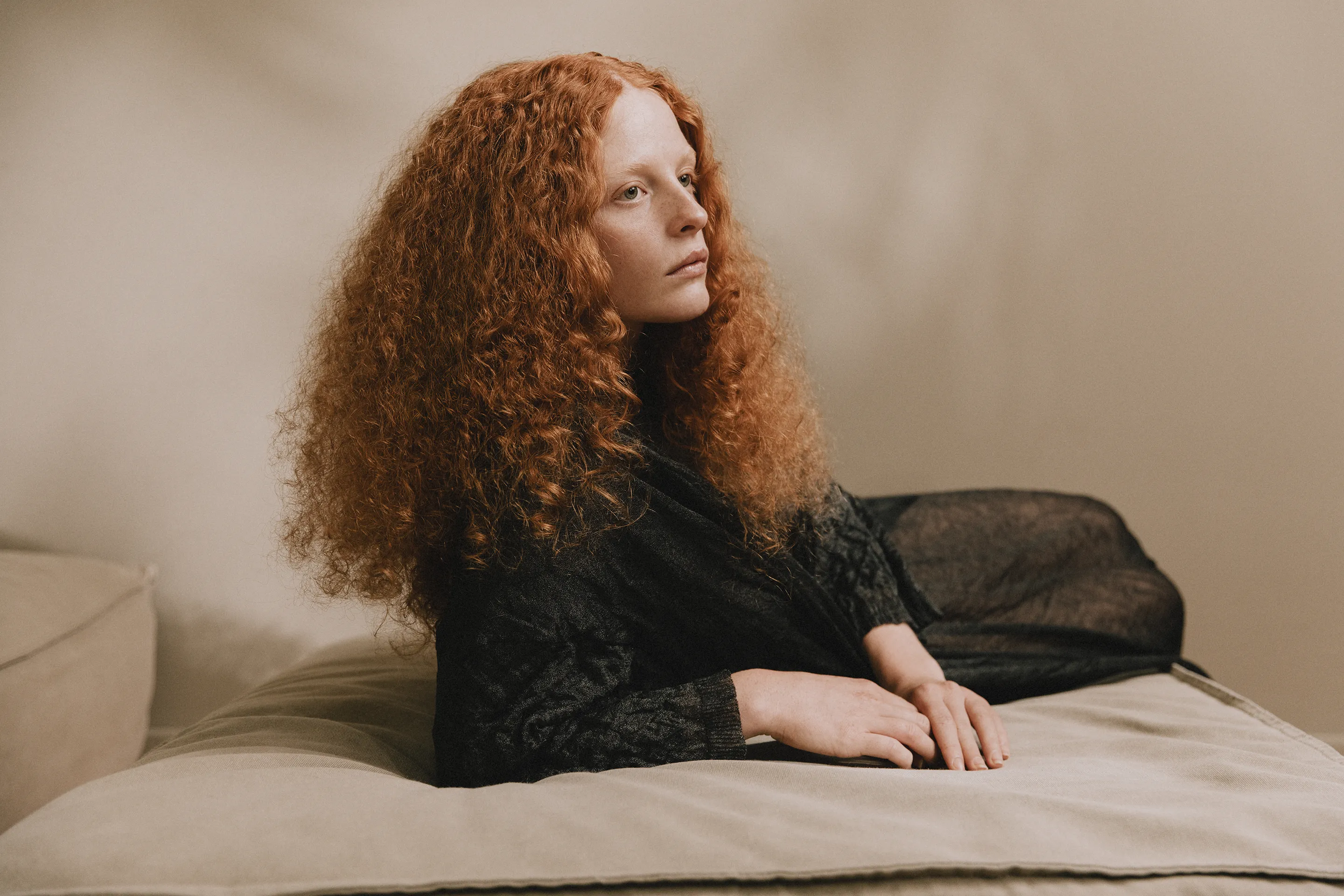 Annapurna SS26 collection model wearing a sheer dark grey textured knit dress reclining on a sofa.