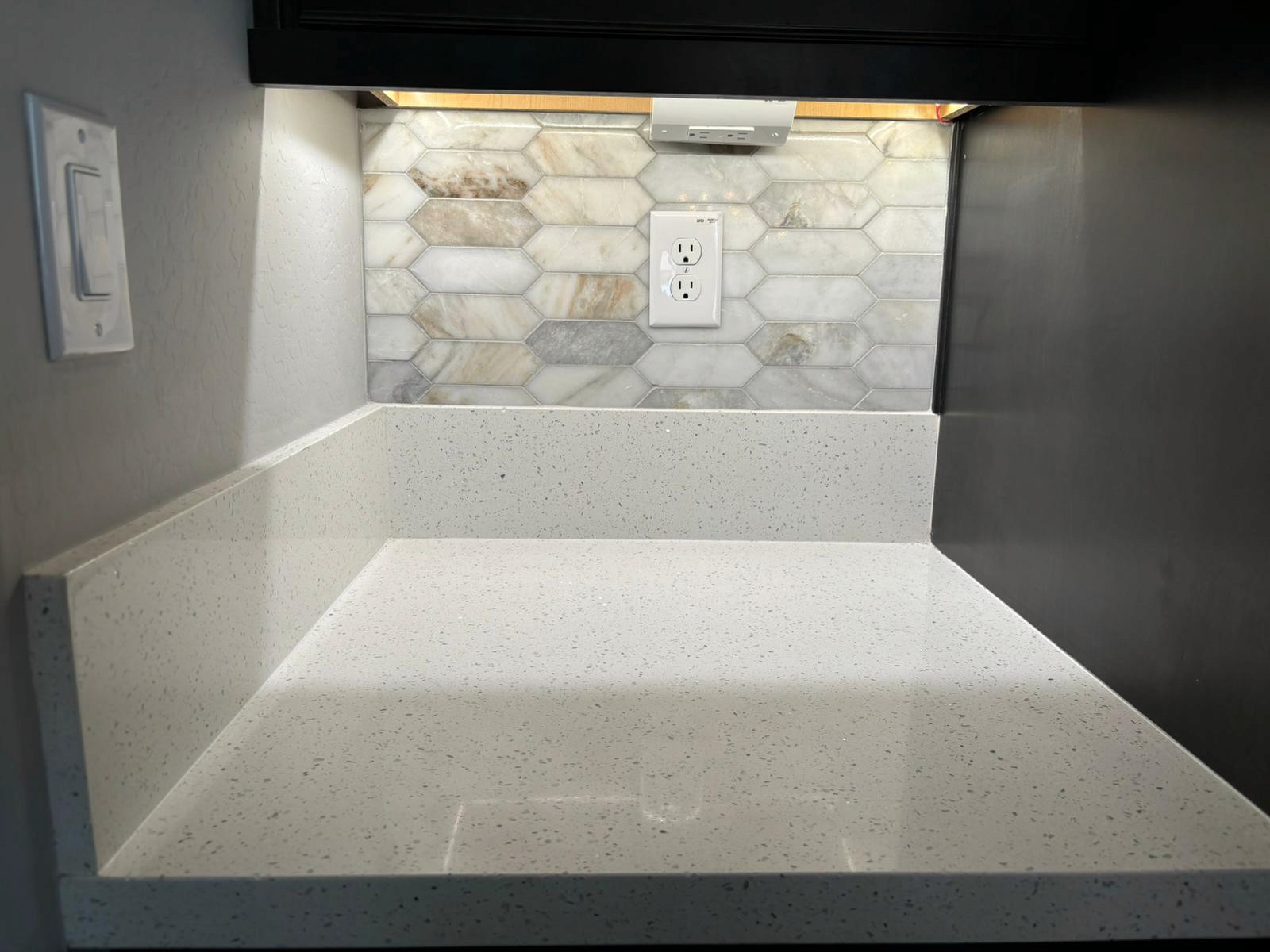 Stylish kitchen with a white countertop, under-cabinet lighting, and a hexagonal tile backsplash.