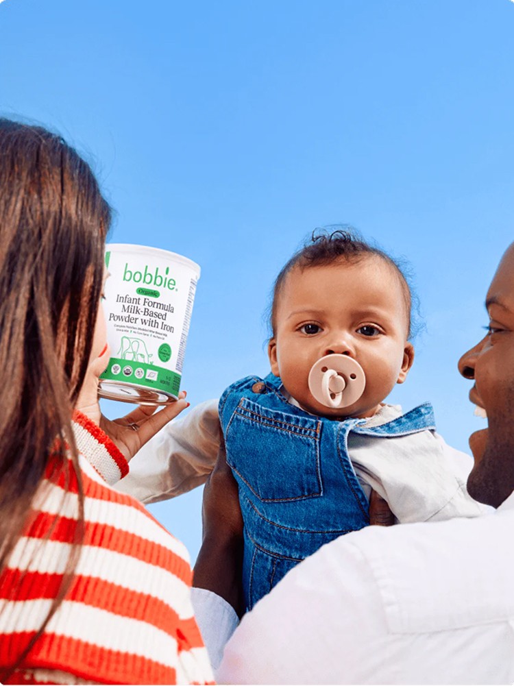A hand pouring cherry vanilla flavoured soda from a colorful can in a tall glass, over a soft sky blue background, with two more cans on the side. Grape and Root Beer flavoured.