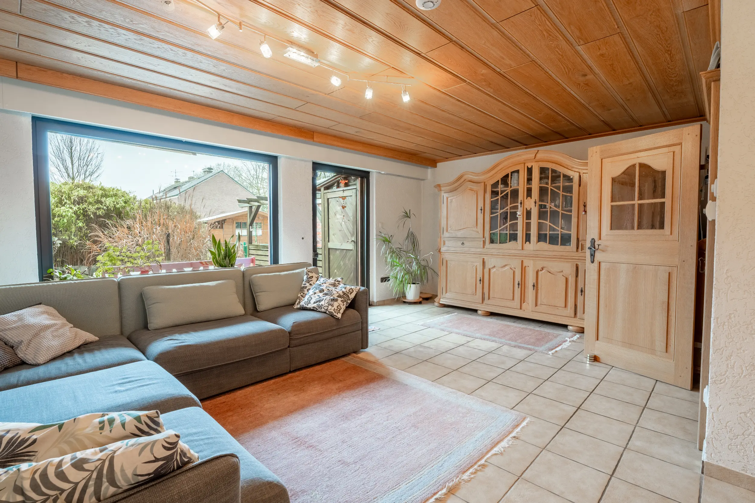 Wohnzimmer im Reihenmittelhaus in Raesfeld mit Holzdecke, großem Fenster, Terrassenzugang, Fliesenboden und gemütlichem Sitzbereich.