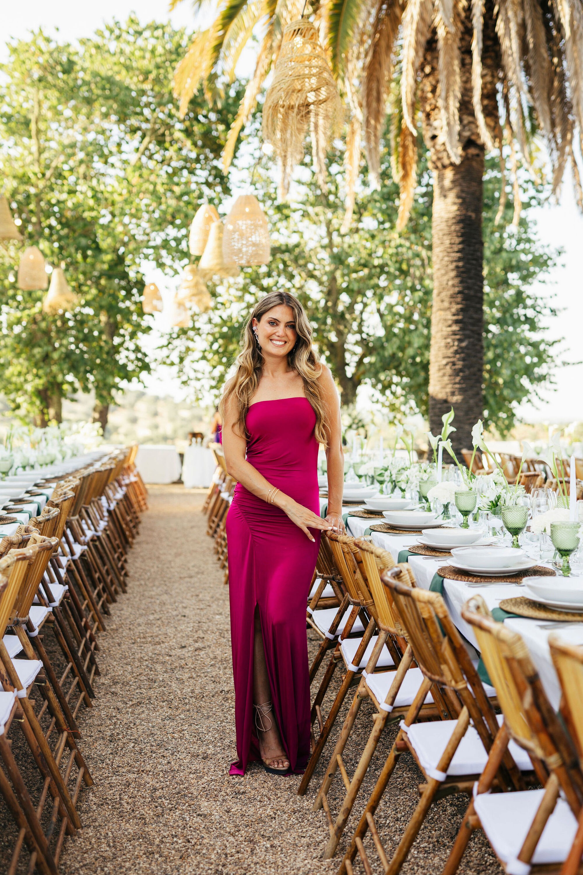 Mariana Degener in a magenta dress beside outdoor wedding tables beneath hanging lanterns